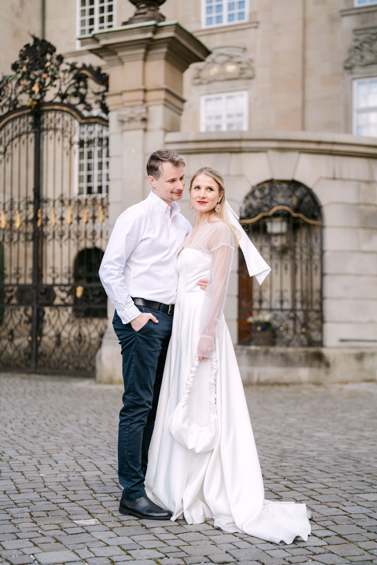 A romantic wedding photoshoot in front of an ornate stone building with decorative gates.