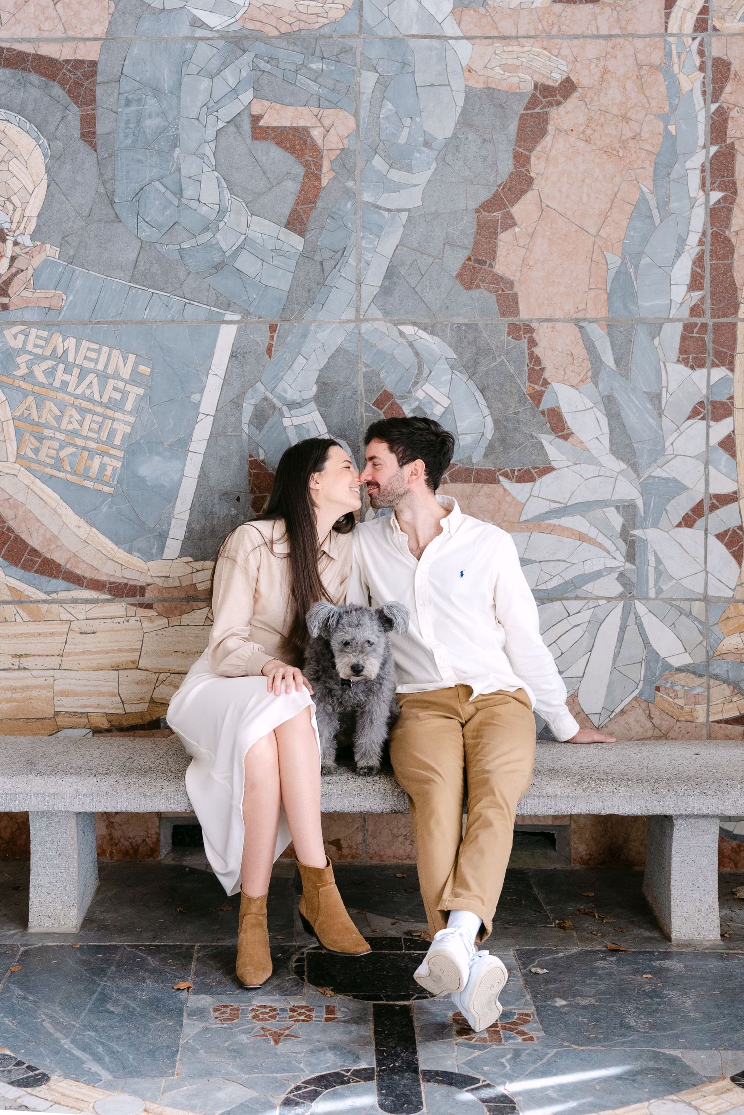A romantic couple sits on a decorative bench with their dog, sharing intimate moments.
