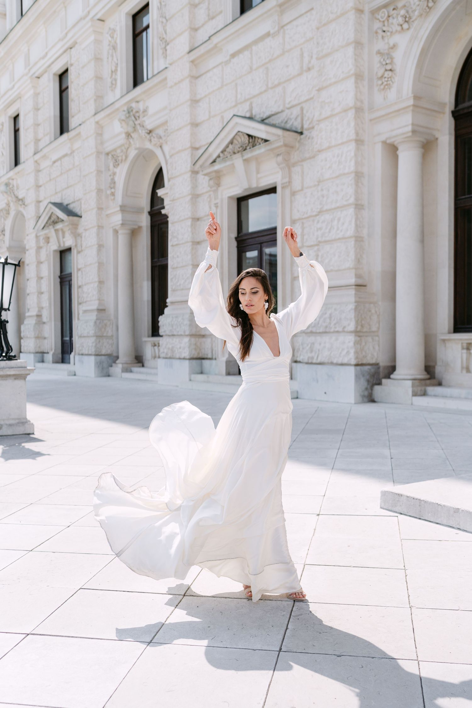 Bride in flowing white dress twirls gracefully against classical architectural backdrop.