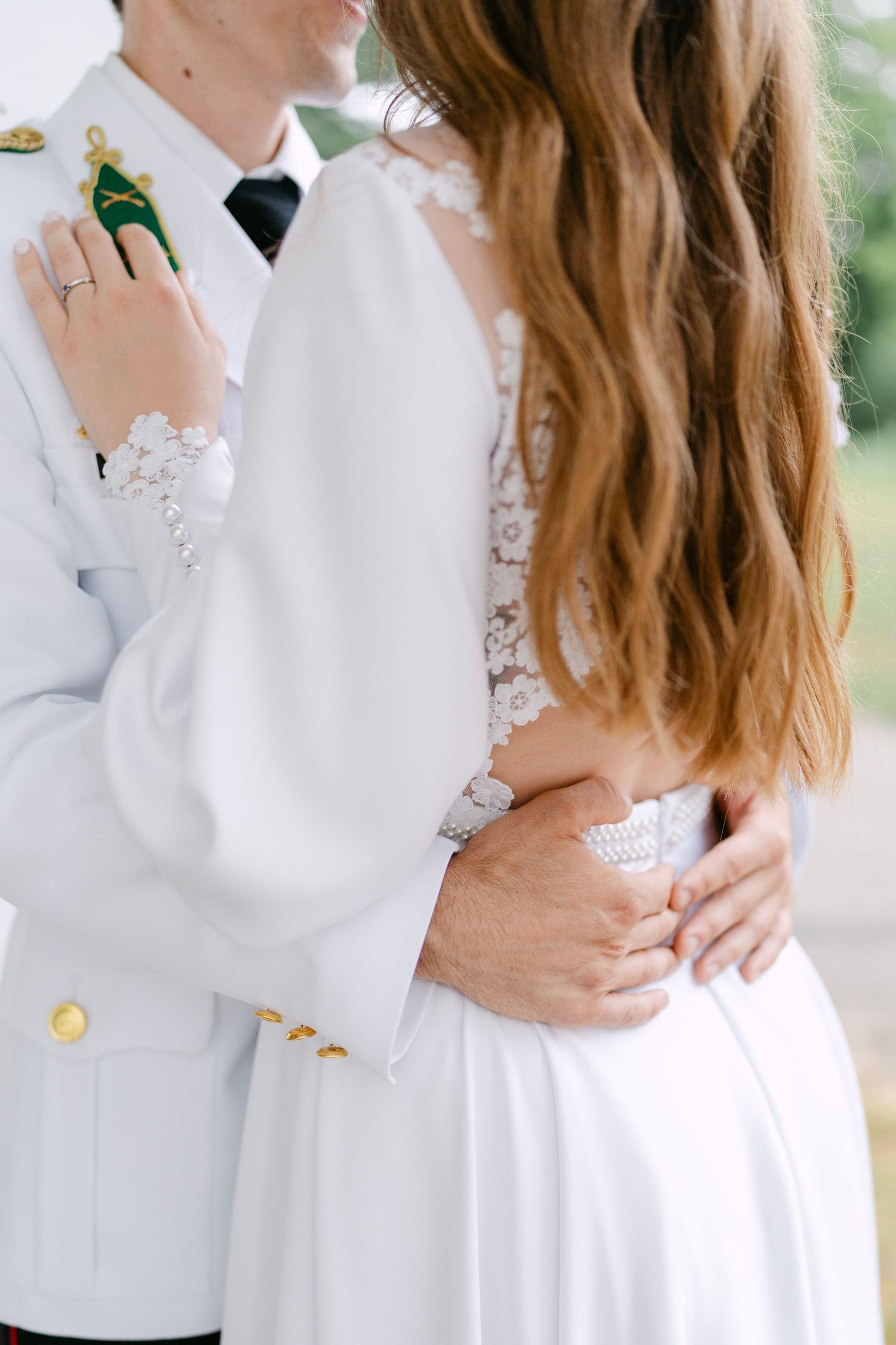Close-up details of military dress whites and lace wedding dress during outdoor photoshoot.