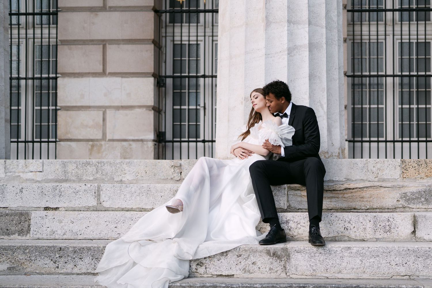 Newlyweds share intimate moments on grand stone steps of historic building.