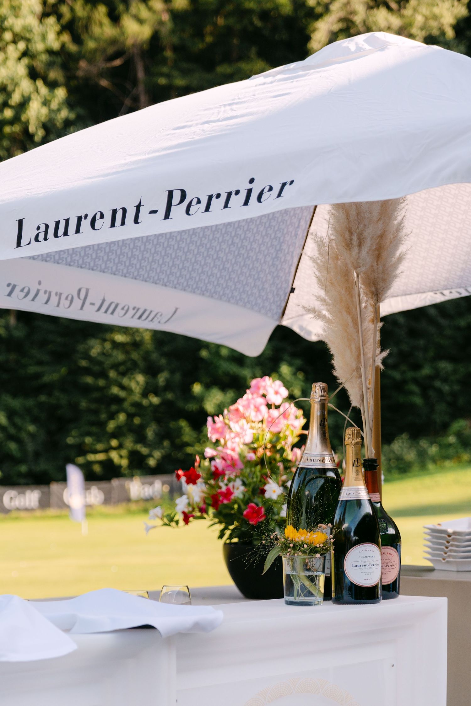 Laurent-Perrier champagne setup with white umbrella, pink flowers and bottles on display table.
