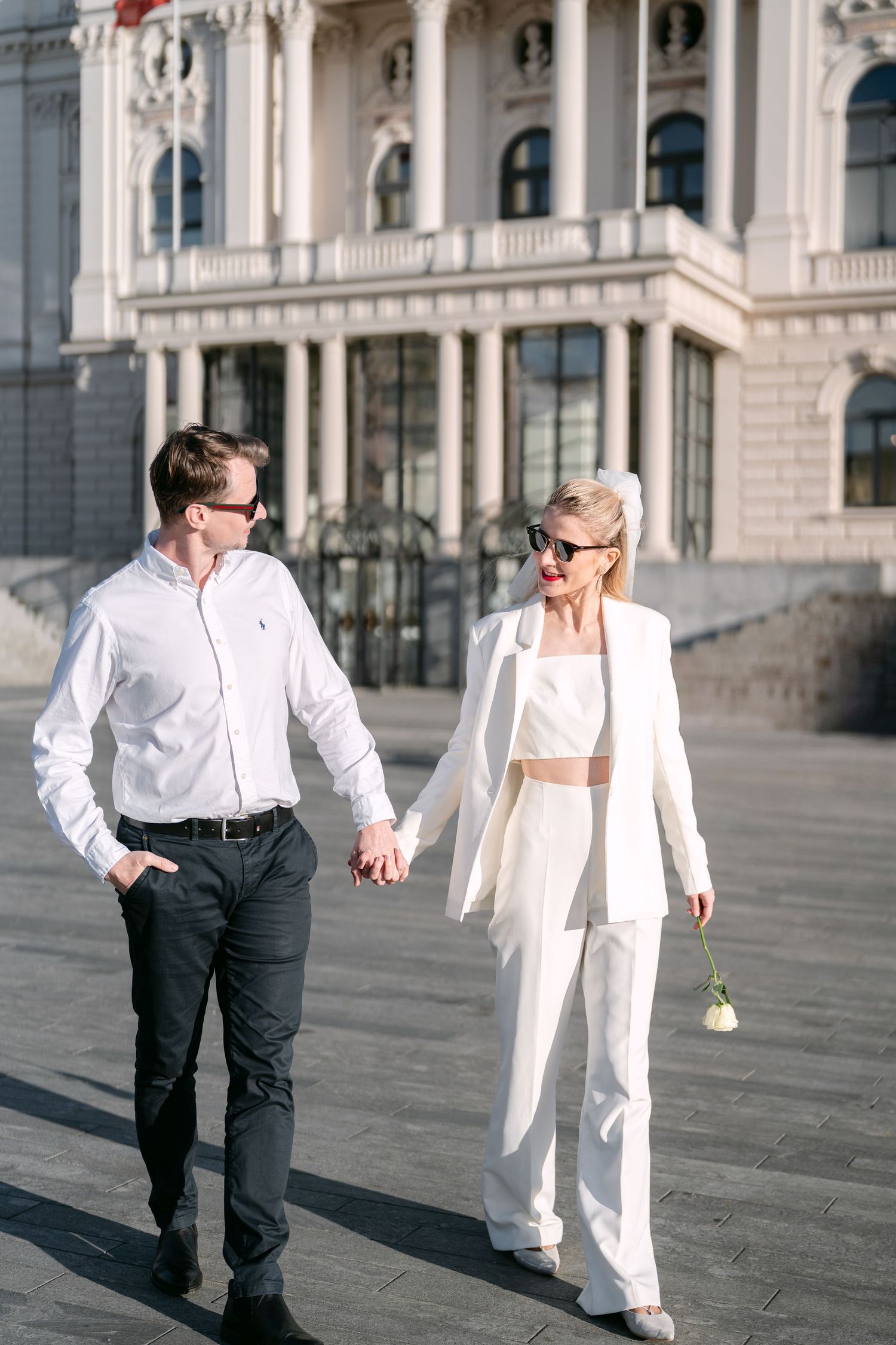 Two people in coordinating white outfits dance playfully outside historic building.