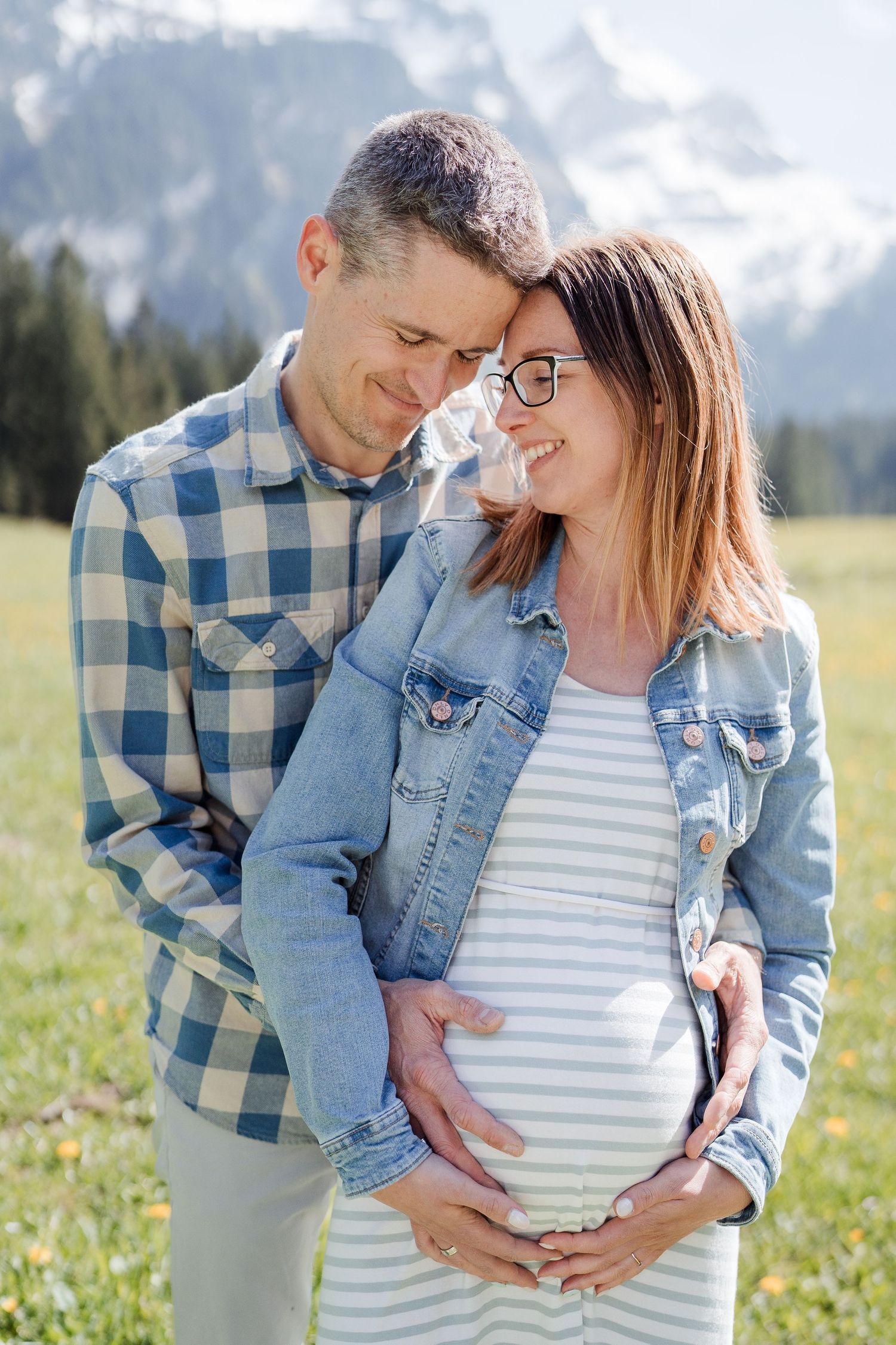 An expectant couple shares an intimate moment in a sunny Alpine meadow.
