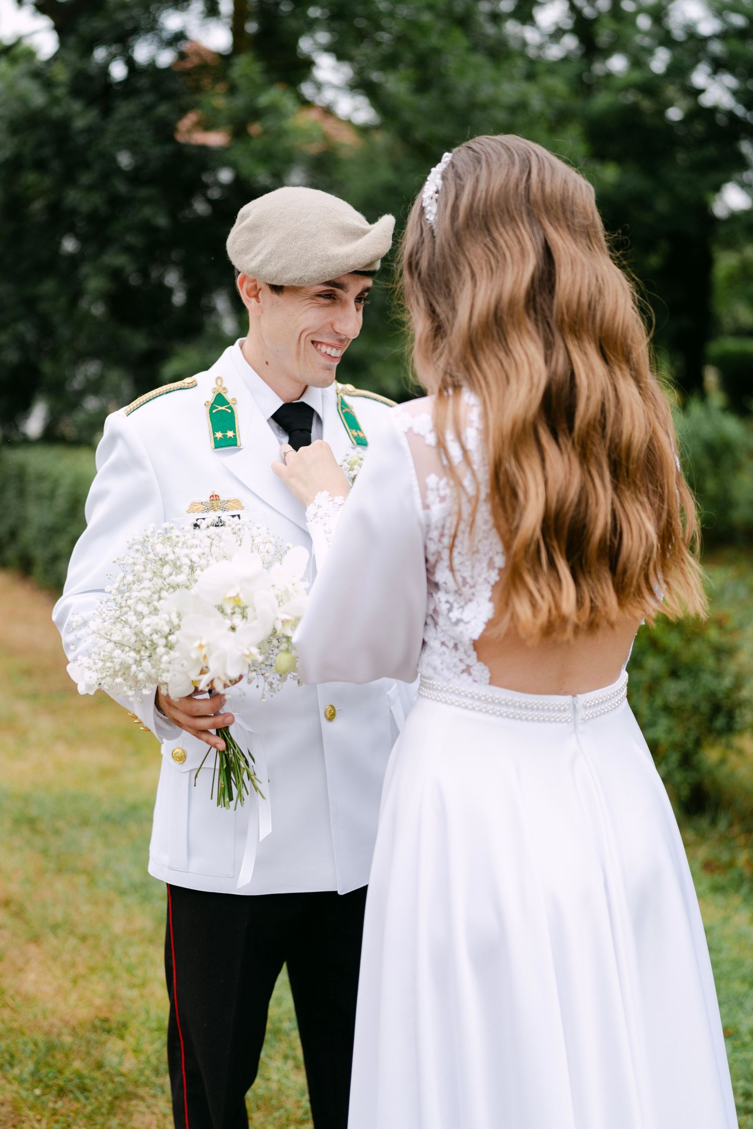Couple in white attire shares romantic moment with baby's breath bouquet outdoors.