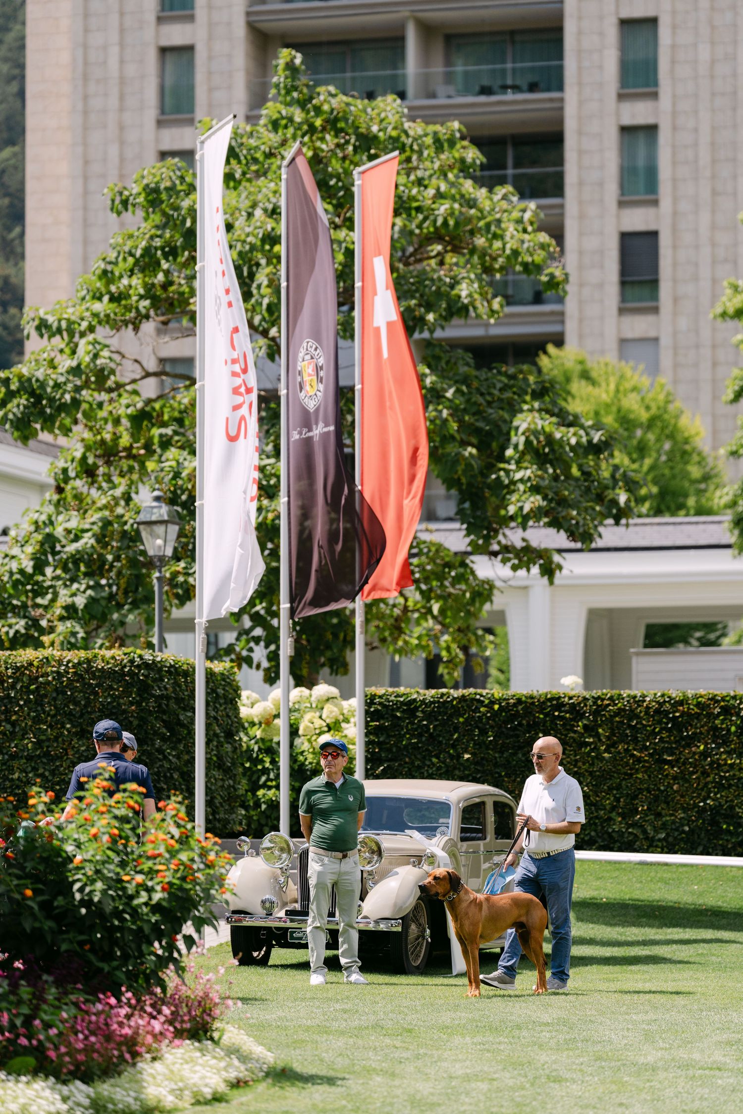 Croquet players practicing on a landscaped lawn with decorative flags and buildings in the background.