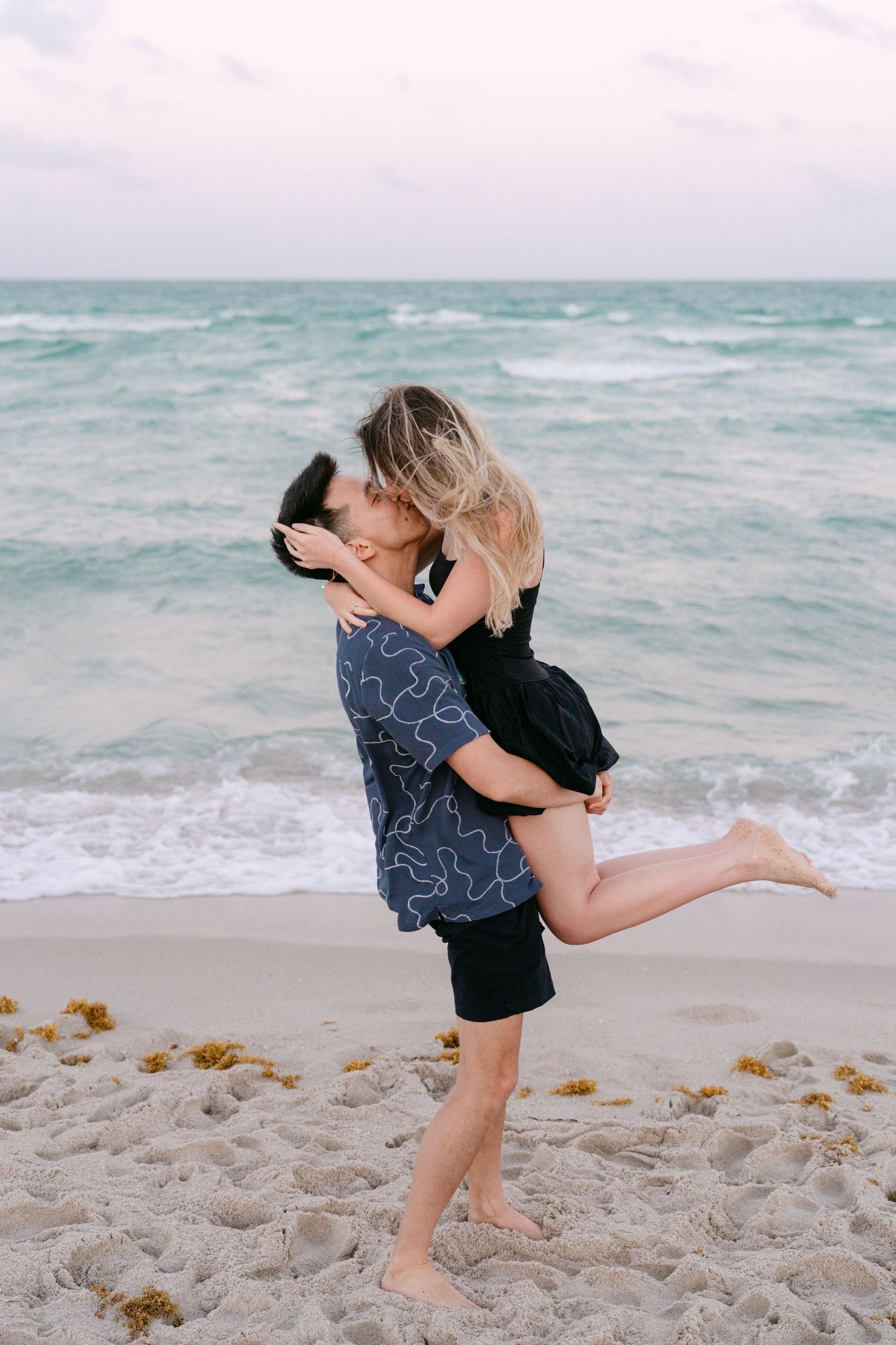A playful couple shares a romantic moment while dancing on the beach at sunset.