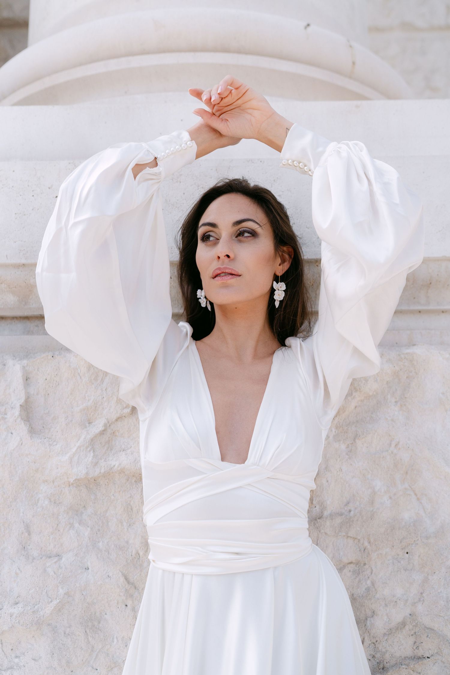 Ethereal bridal portraits showcase flowing white dress with dramatic sleeves against stone architecture.