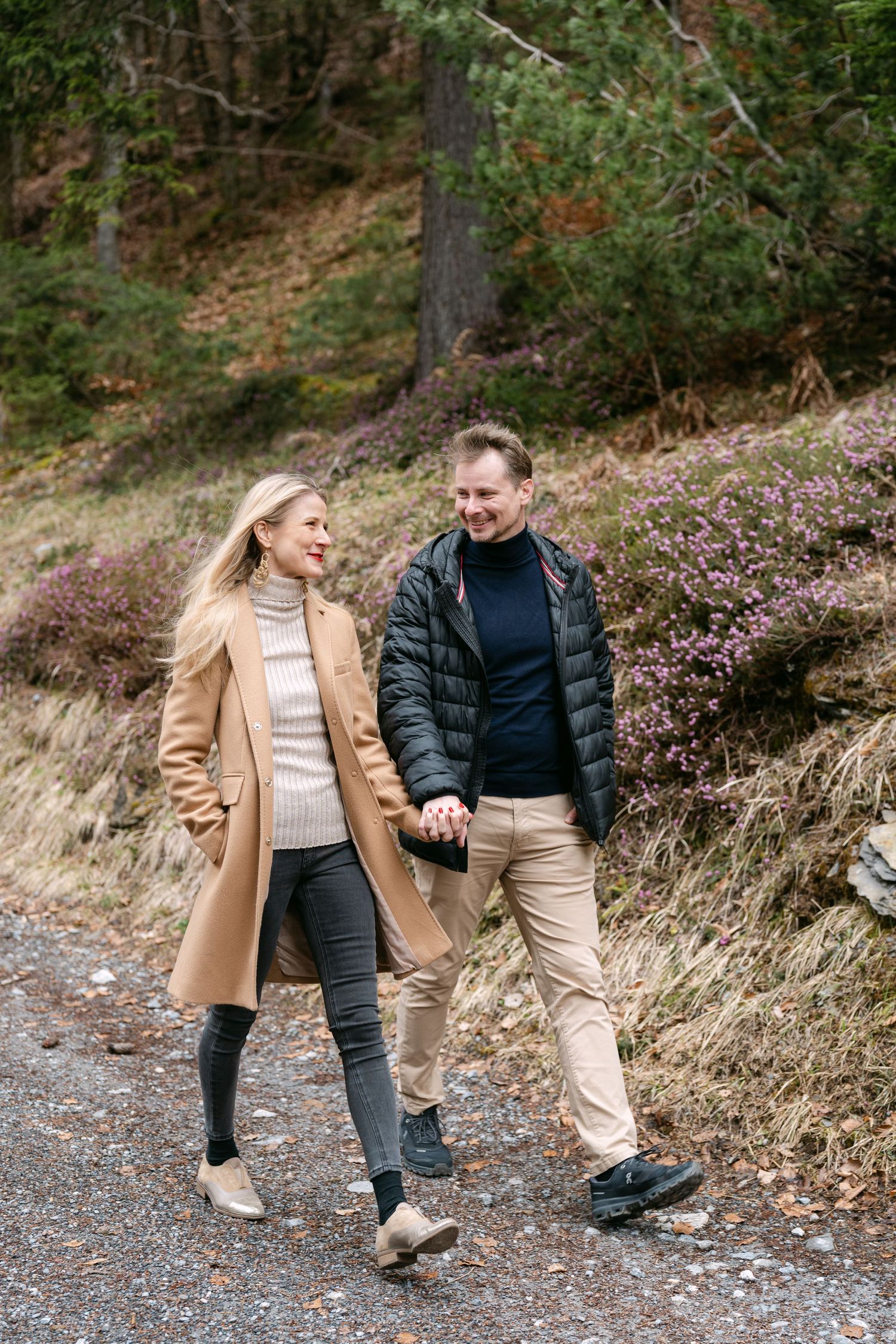 A couple walks along a forest trail in autumn, wearing casual outerwear.