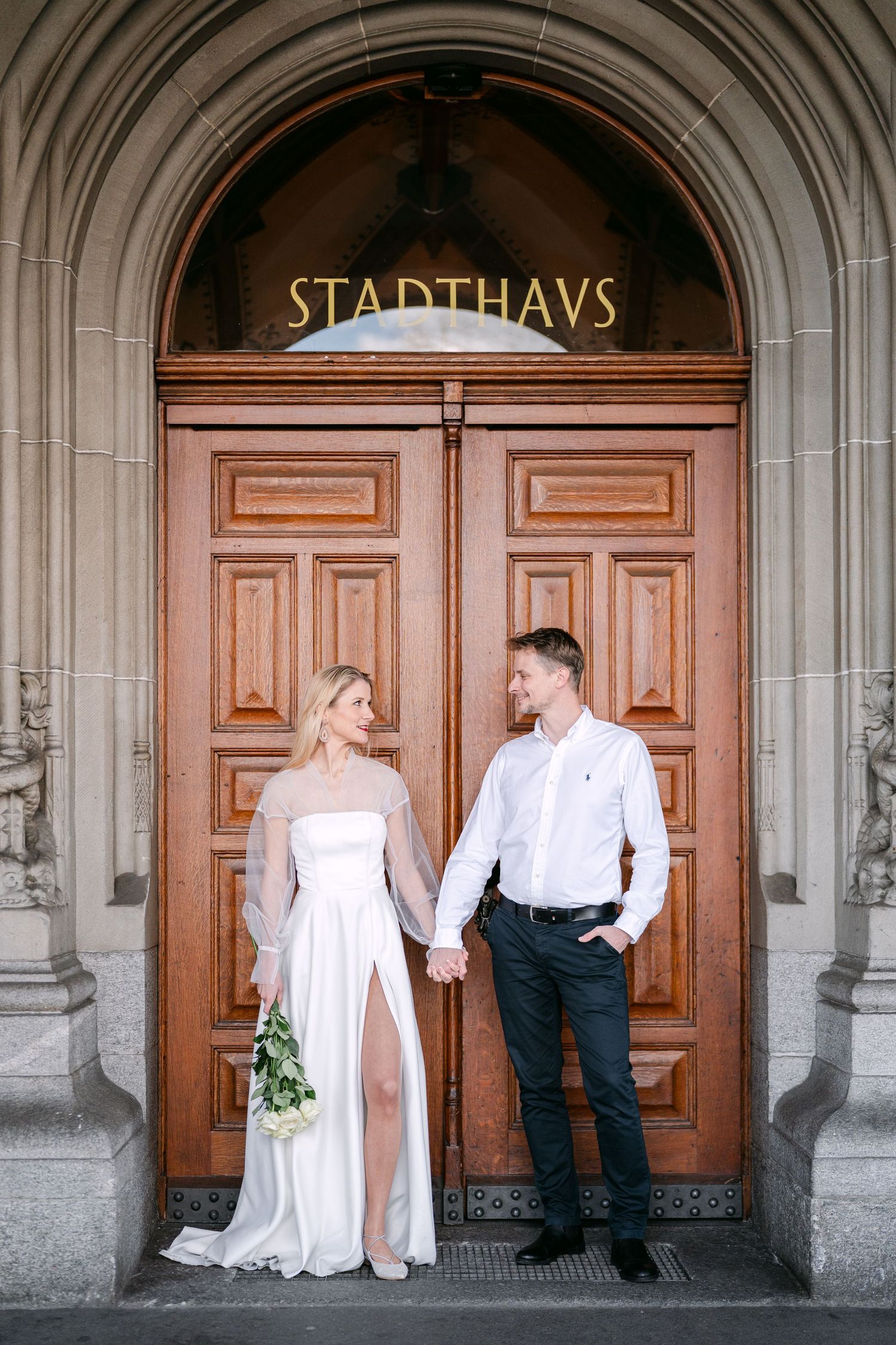 Wedding couple poses in front of historic Stadthaus building with wooden doors.