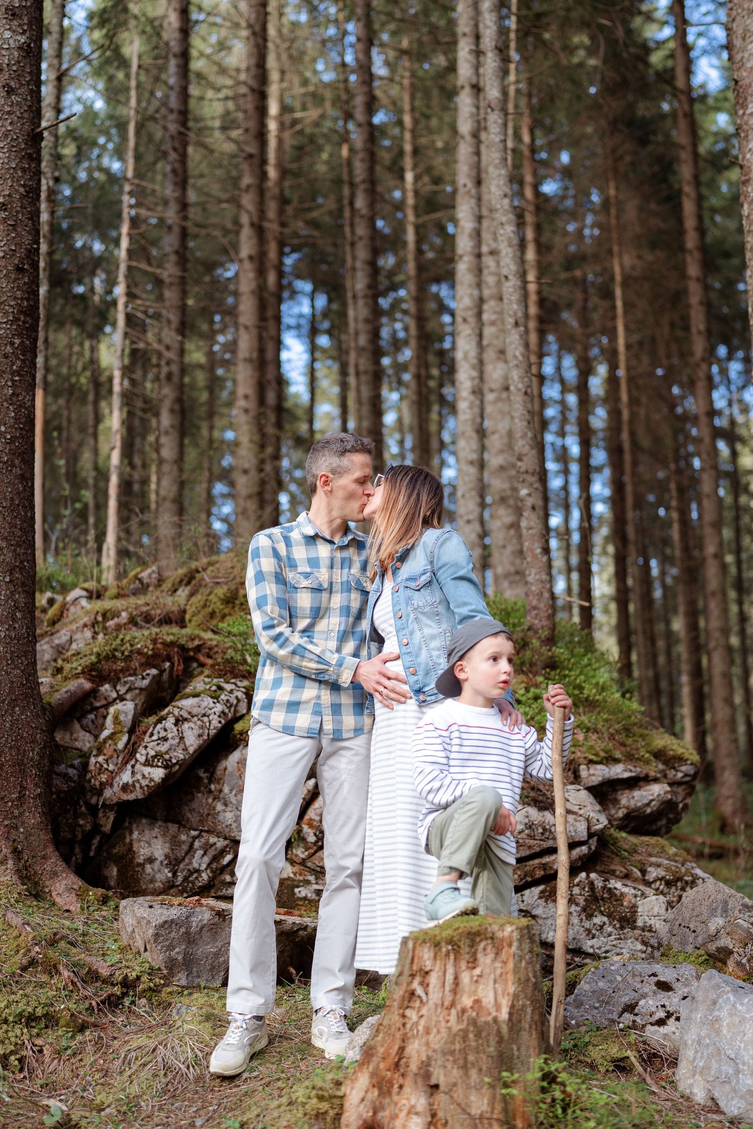 Family posing on rocky forest terrain surrounded by tall pine trees.