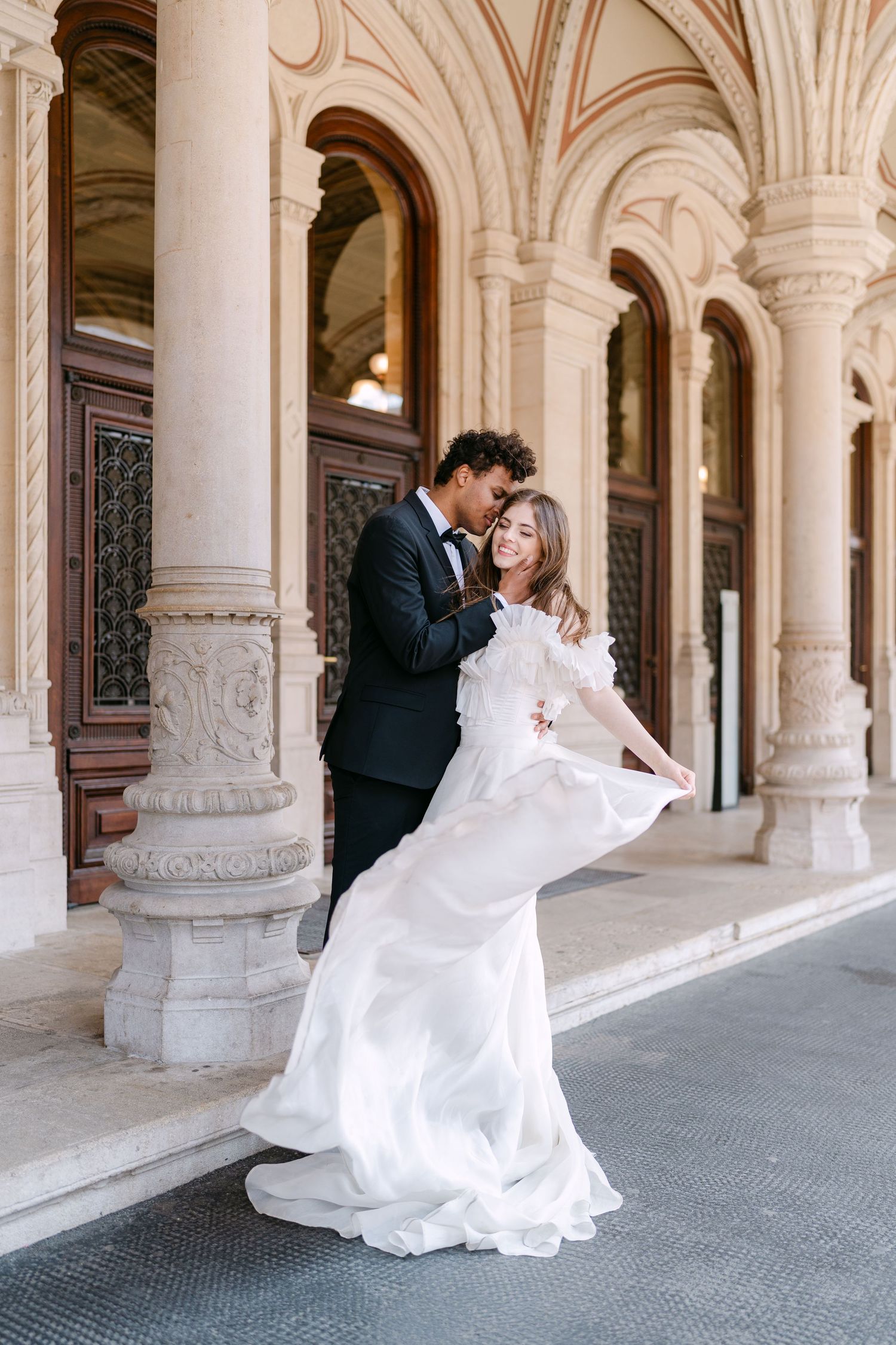 Wedding photoshoot under ornate stone colonnade with dramatic dress movement.