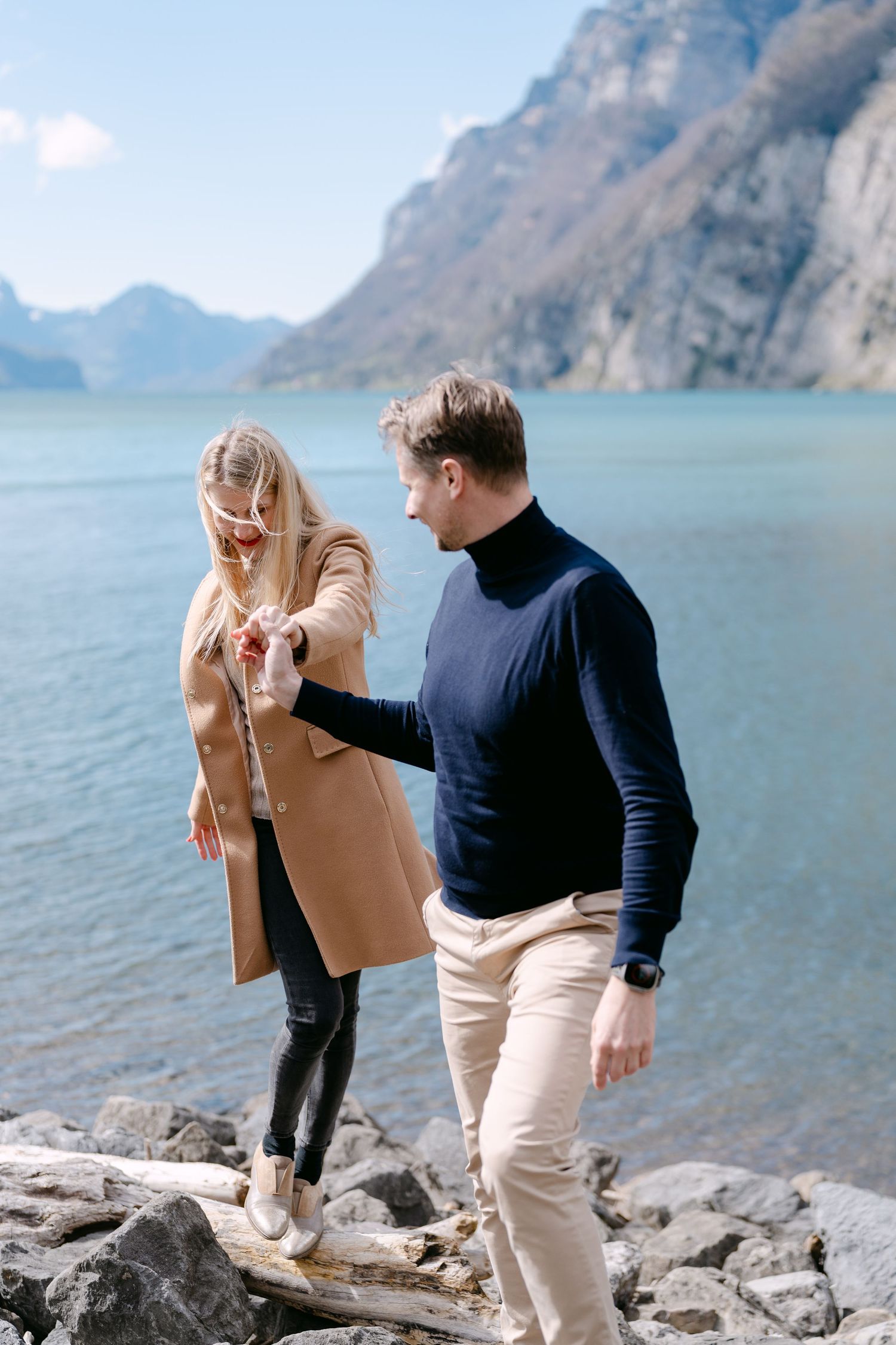 Couple enjoying a scenic mountain lake view while dancing on rocky shoreline.