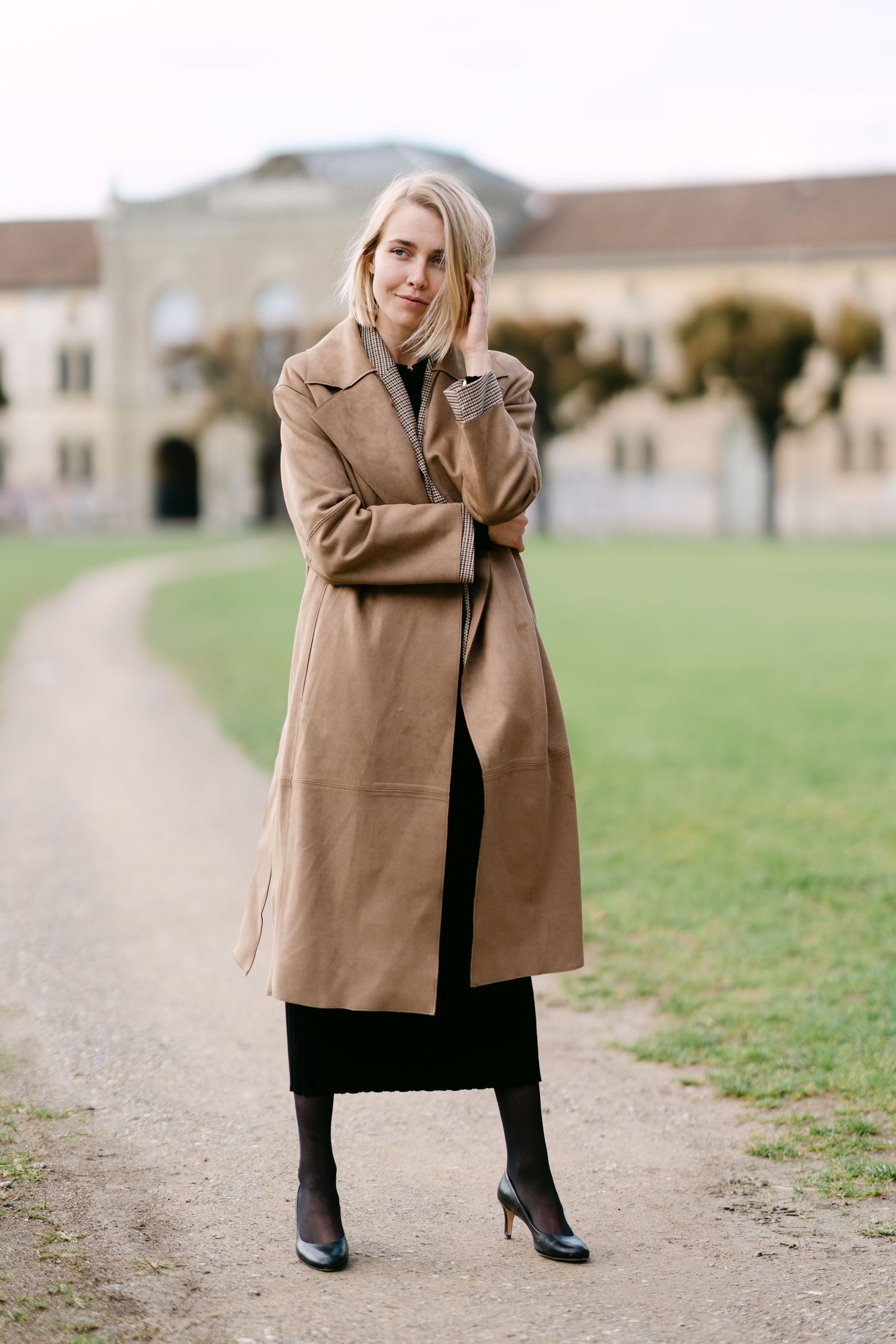 Outdoor fashion photography featuring a classic camel coat on a gravel path.