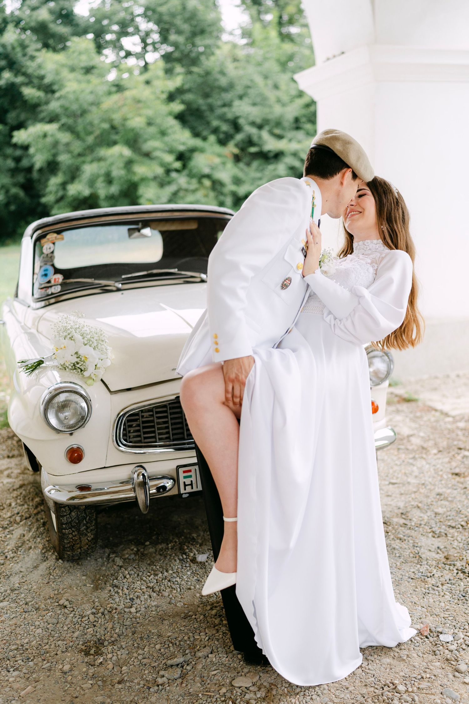 A romantic scene with white attire and a classic car against an elegant white building.