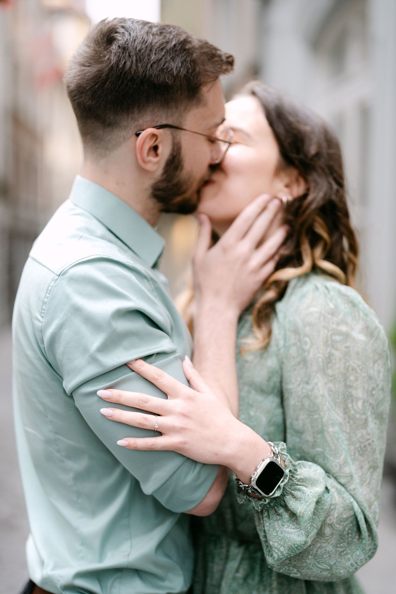 A couple shares a passionate kiss while wearing coordinating mint green outfits on a city street.