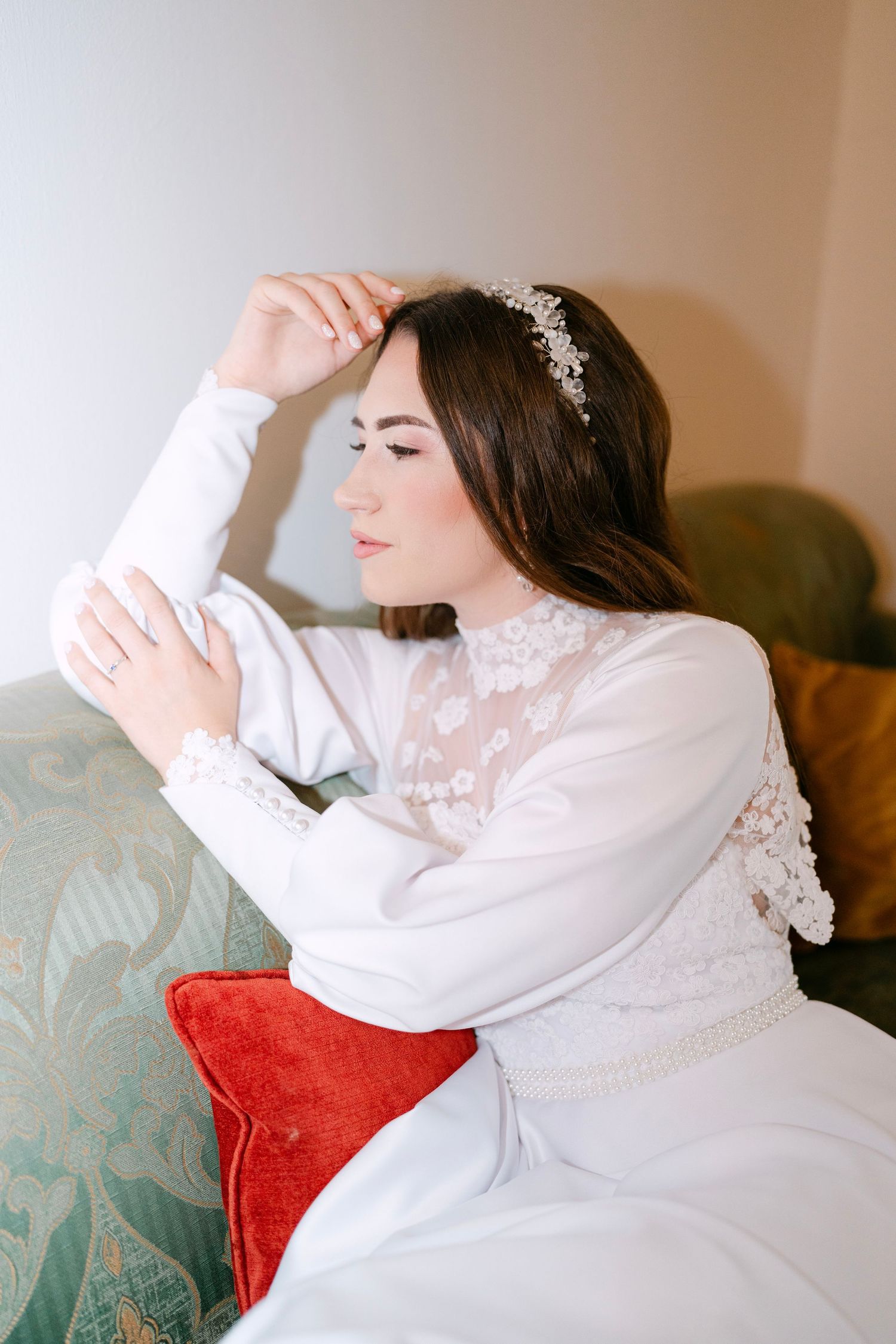 Person in white dress reclines elegantly on teal couch with red pillow.