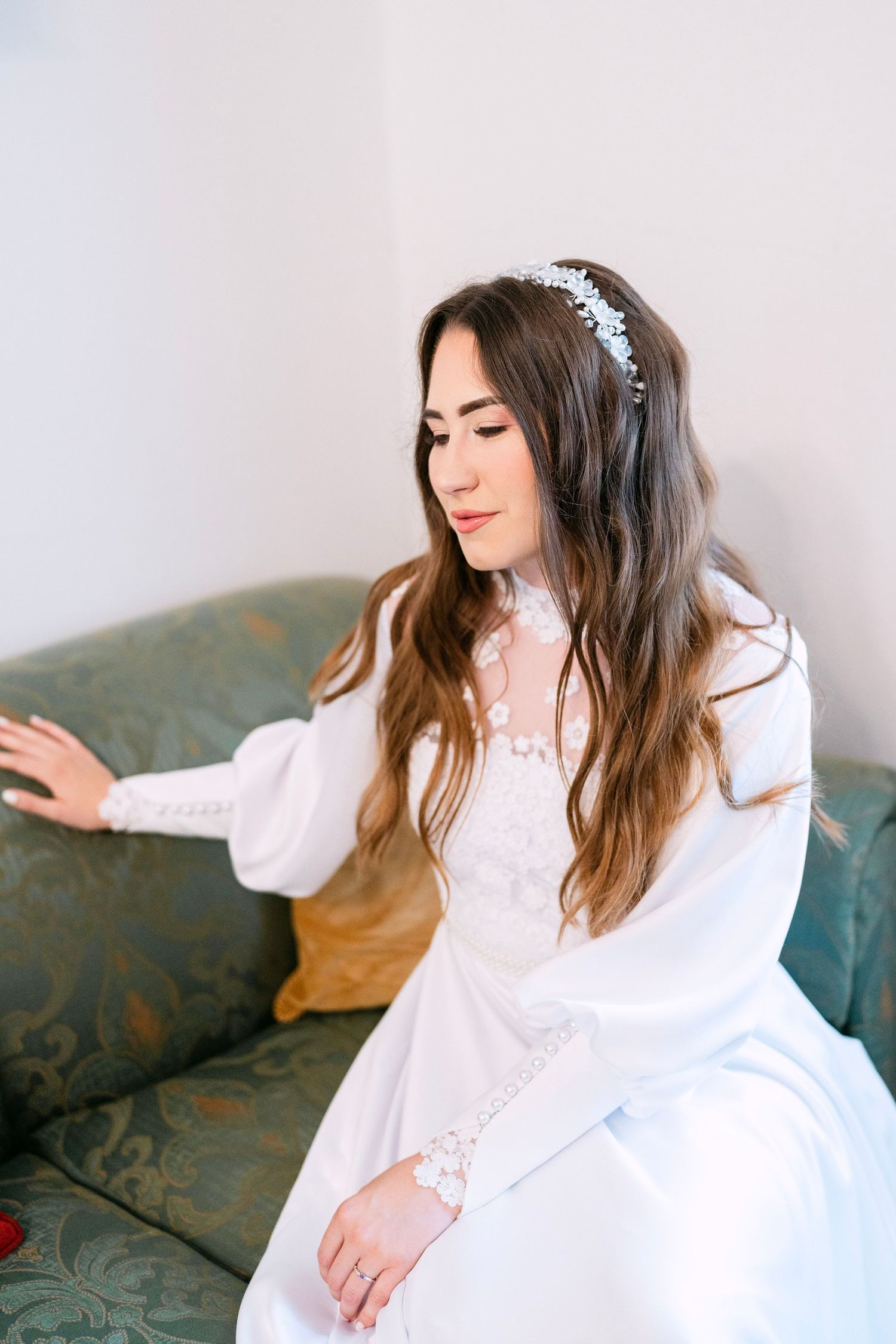 Person in white lace dress relaxes on vintage couch during bridal photoshoot.