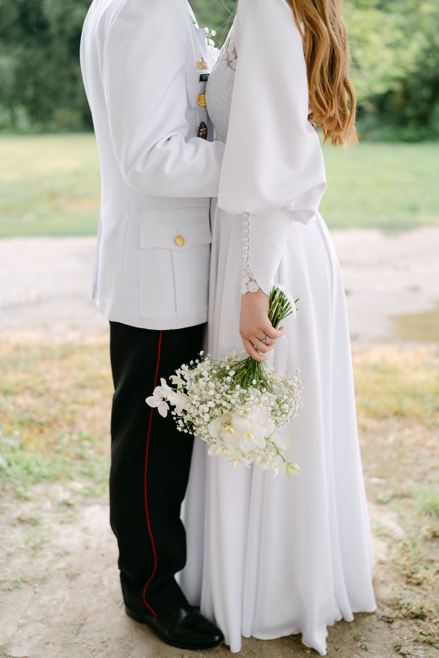 A tender moment between a couple in white and military formal wear holding baby's breath flowers.