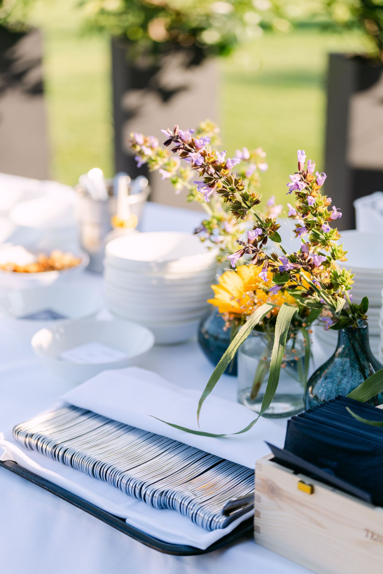 Table settings with blue vases holding yellow and purple flowers on white linens.