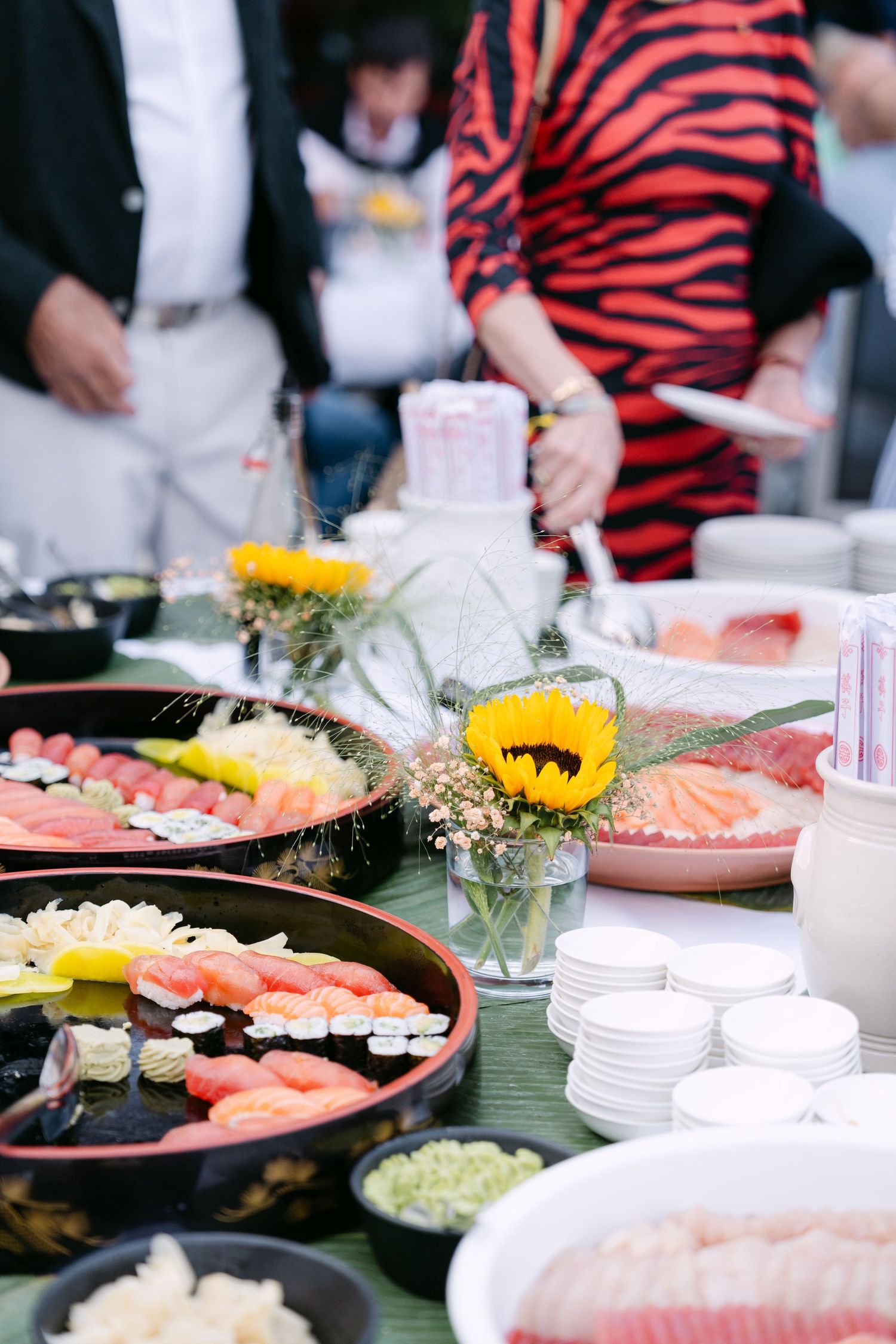 Colorful sushi and appetizer platters arranged on a buffet table with decorative flowers.