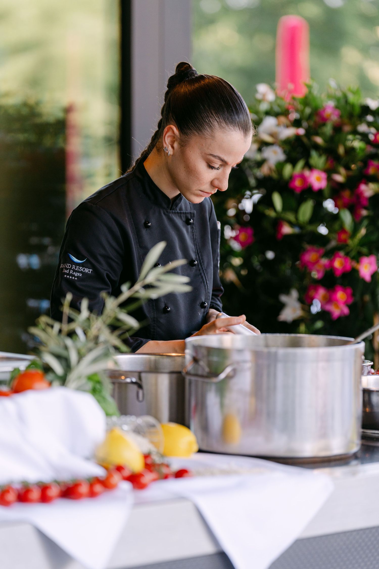 Chef preparing ingredients at an outdoor cooking station with pink flowers in background.