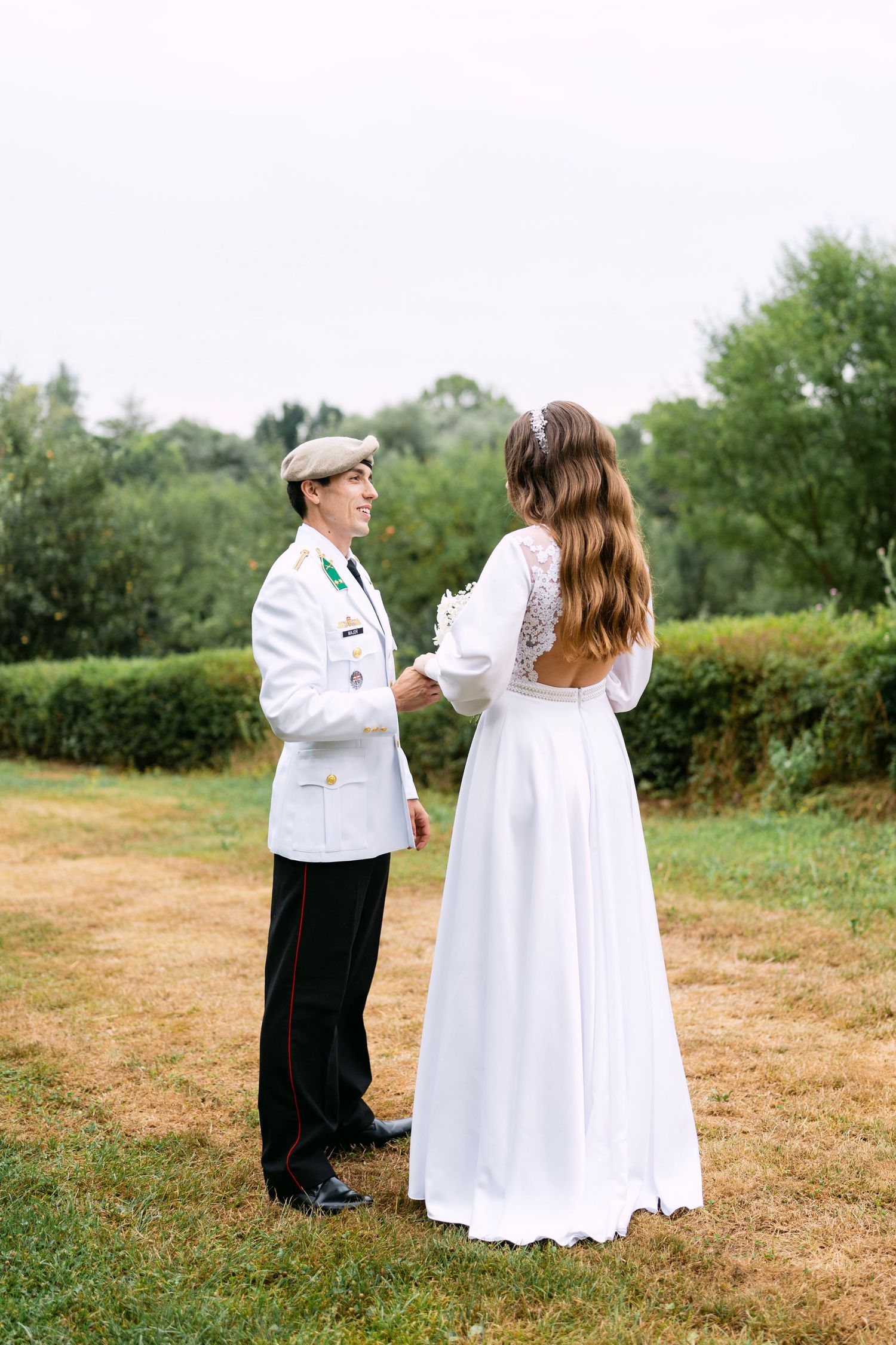 Couple in white clothing stands together on grassy field.