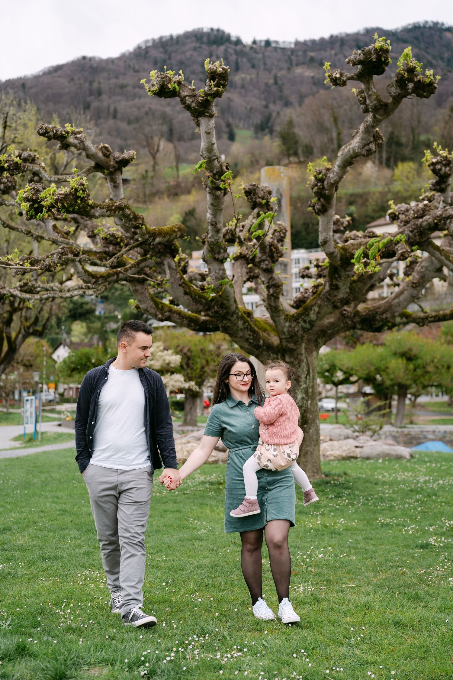 Family enjoying a playful moment in a grassy field with blooming trees.