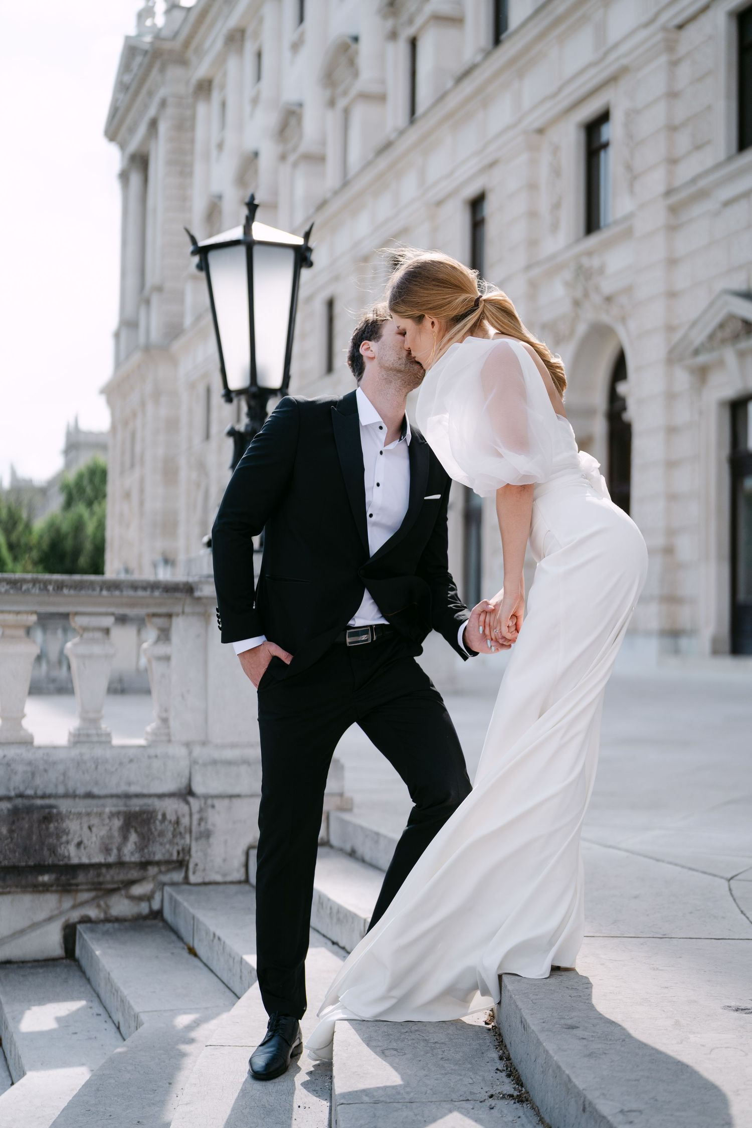 Elegant wedding couple in black and white attire posing playfully on grand stone steps.