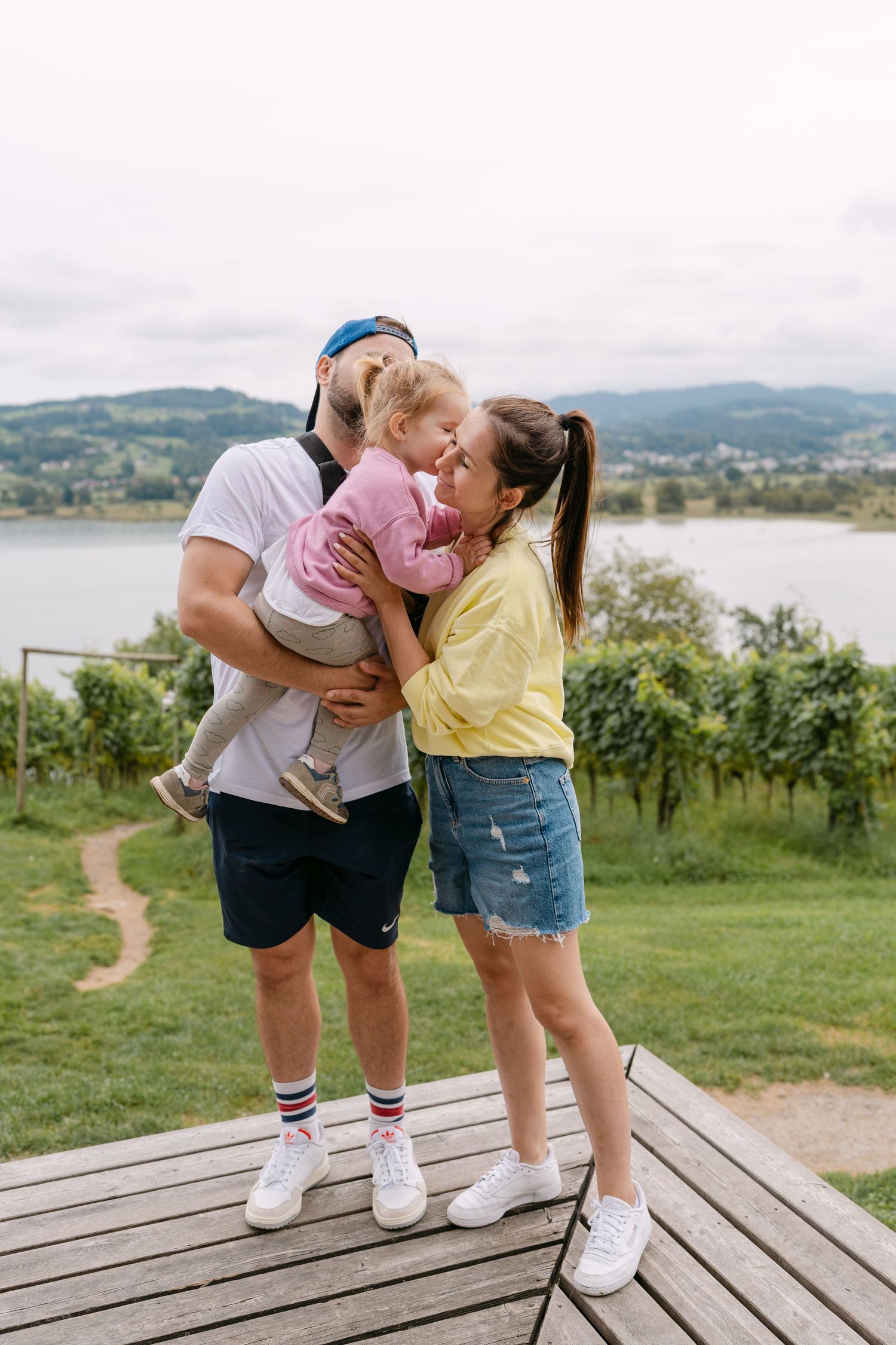 Family sharing intimate moments on wooden deck with vineyard and lake views.