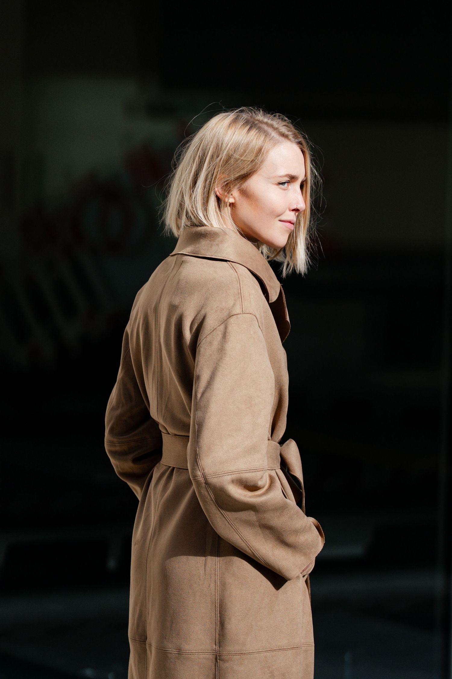 Dramatic lighting highlights a tan coat in an architectural setting.
