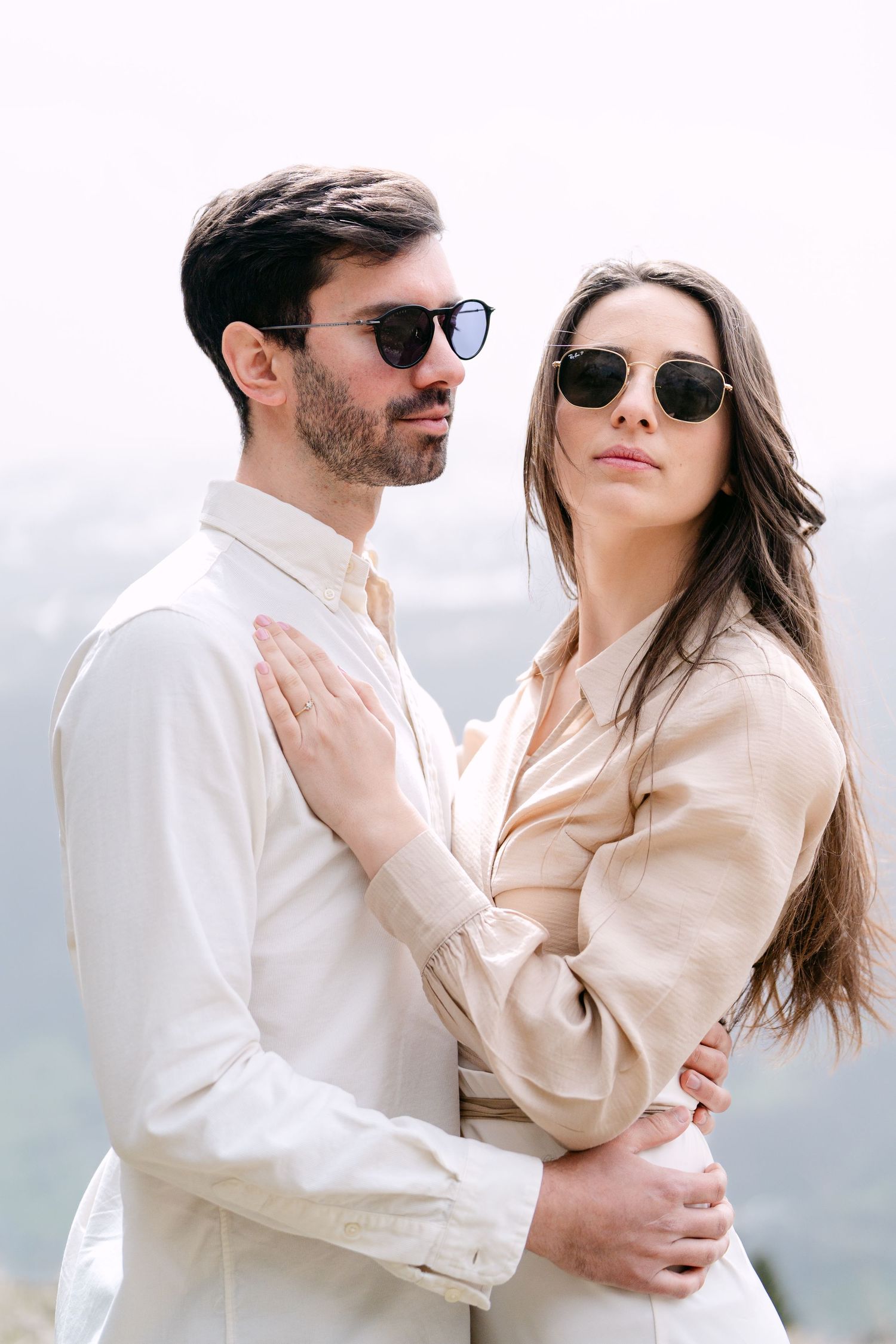 A romantic couple in neutral tones embraces against a bright mountain backdrop.