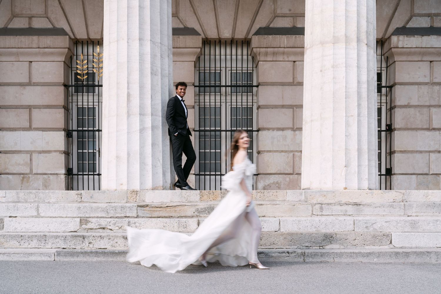 Bride and groom walk along elegant columned building with flowing white dress.