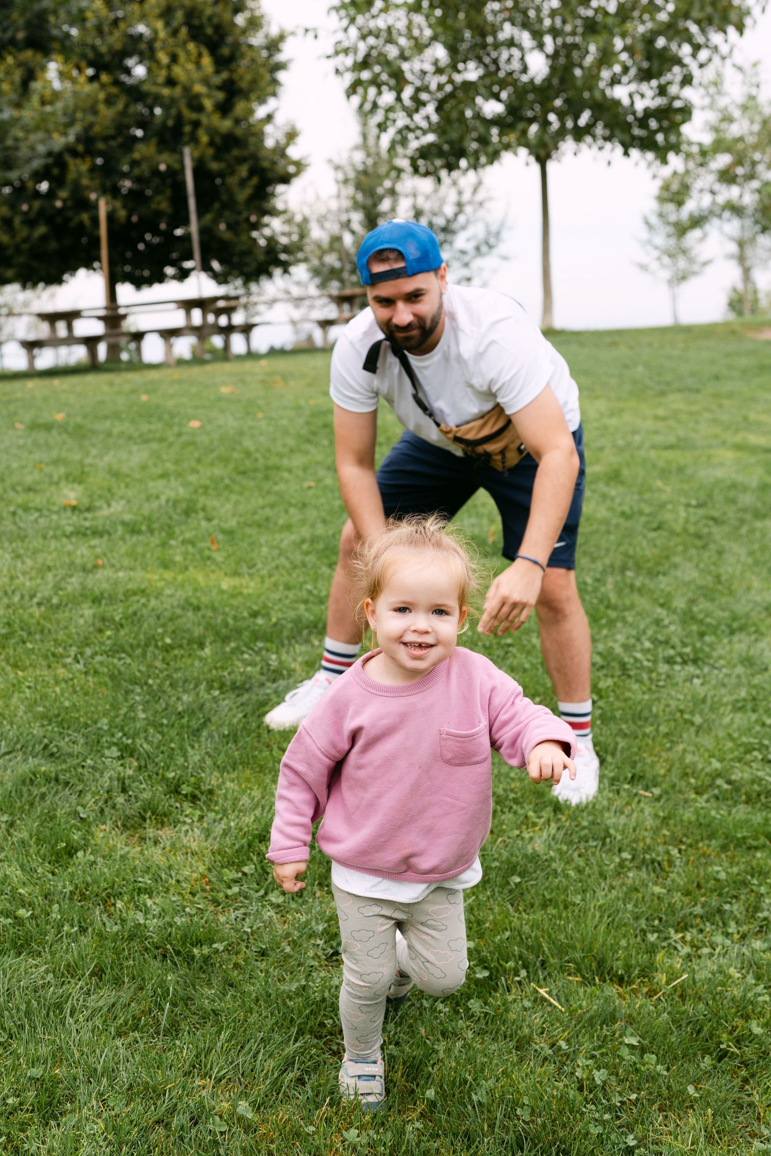 A toddler in a pink sweater running and playing on green grass.