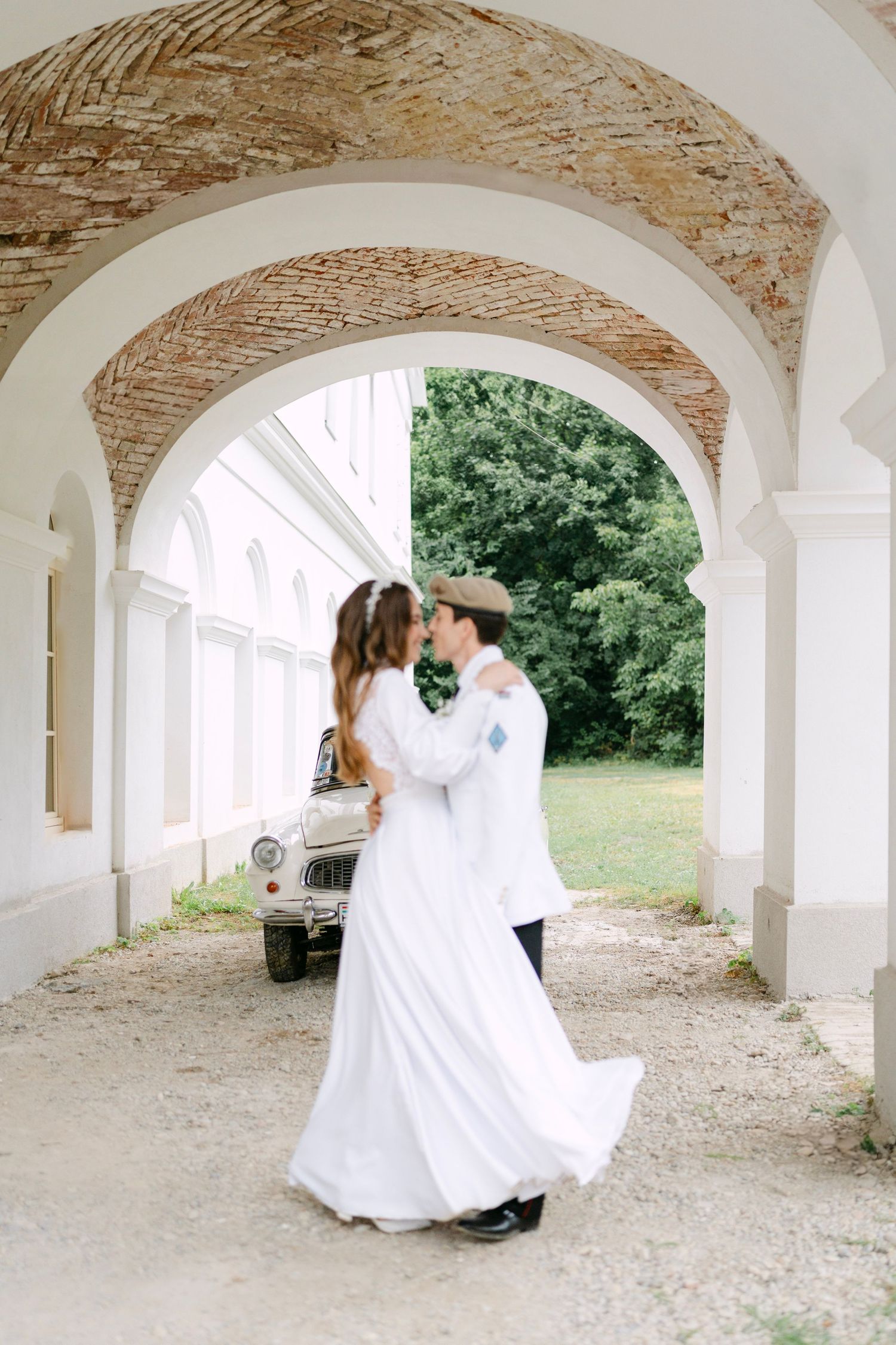 A couple dancing under beautiful brick and white archways near a vintage automobile.