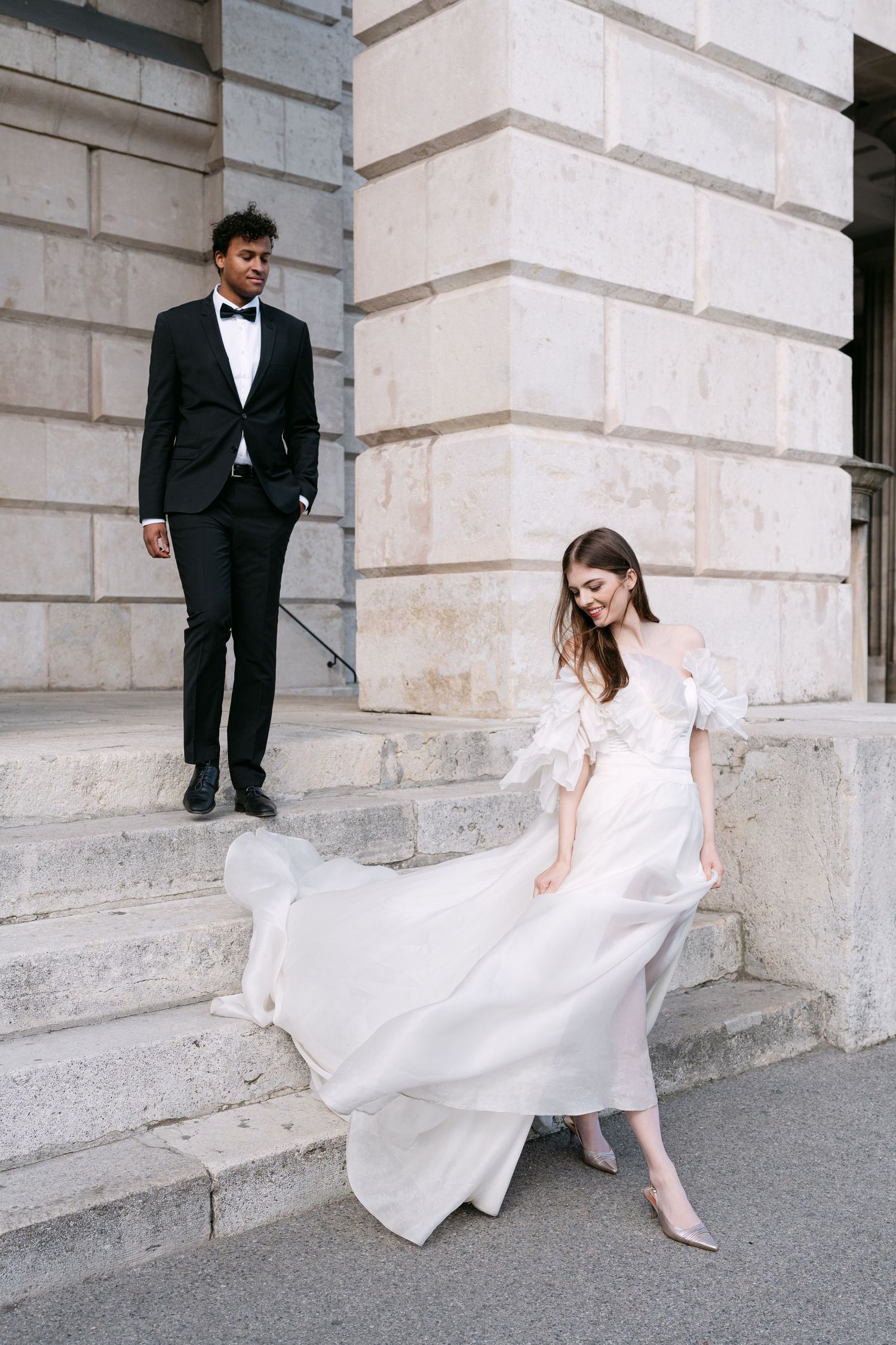 Bride in flowing white gown twirls gracefully against classical stone architecture.