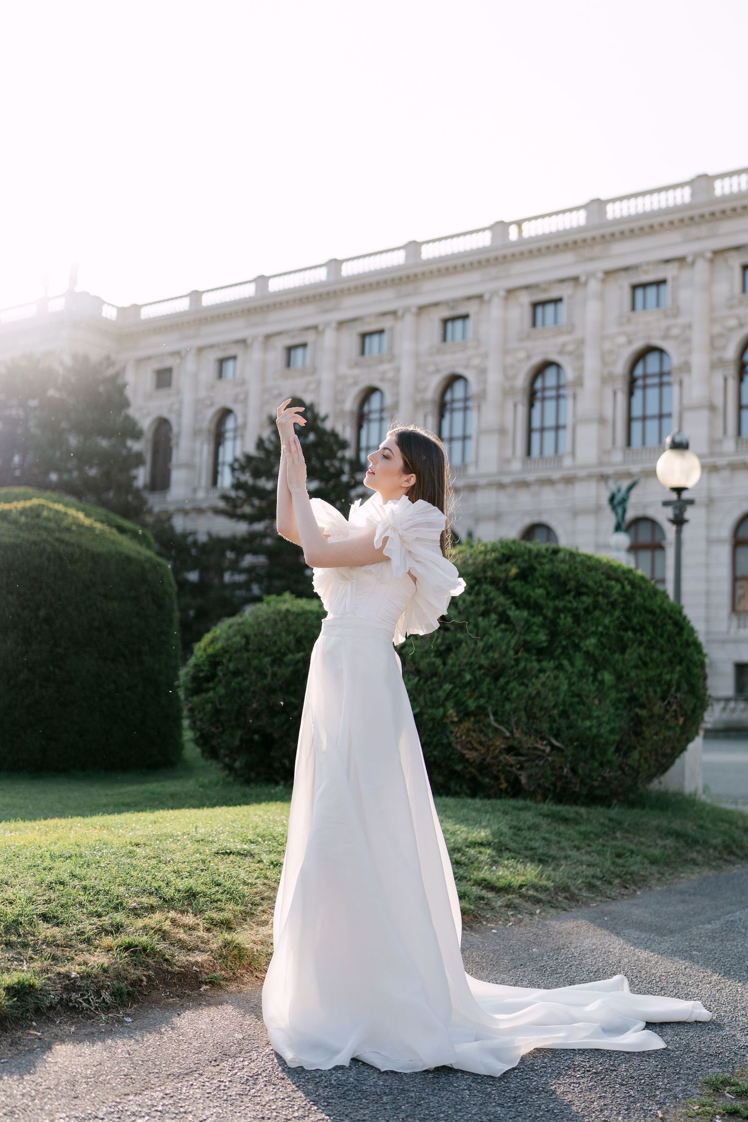 Bride in flowing white gown twirls joyfully against historic European architecture.