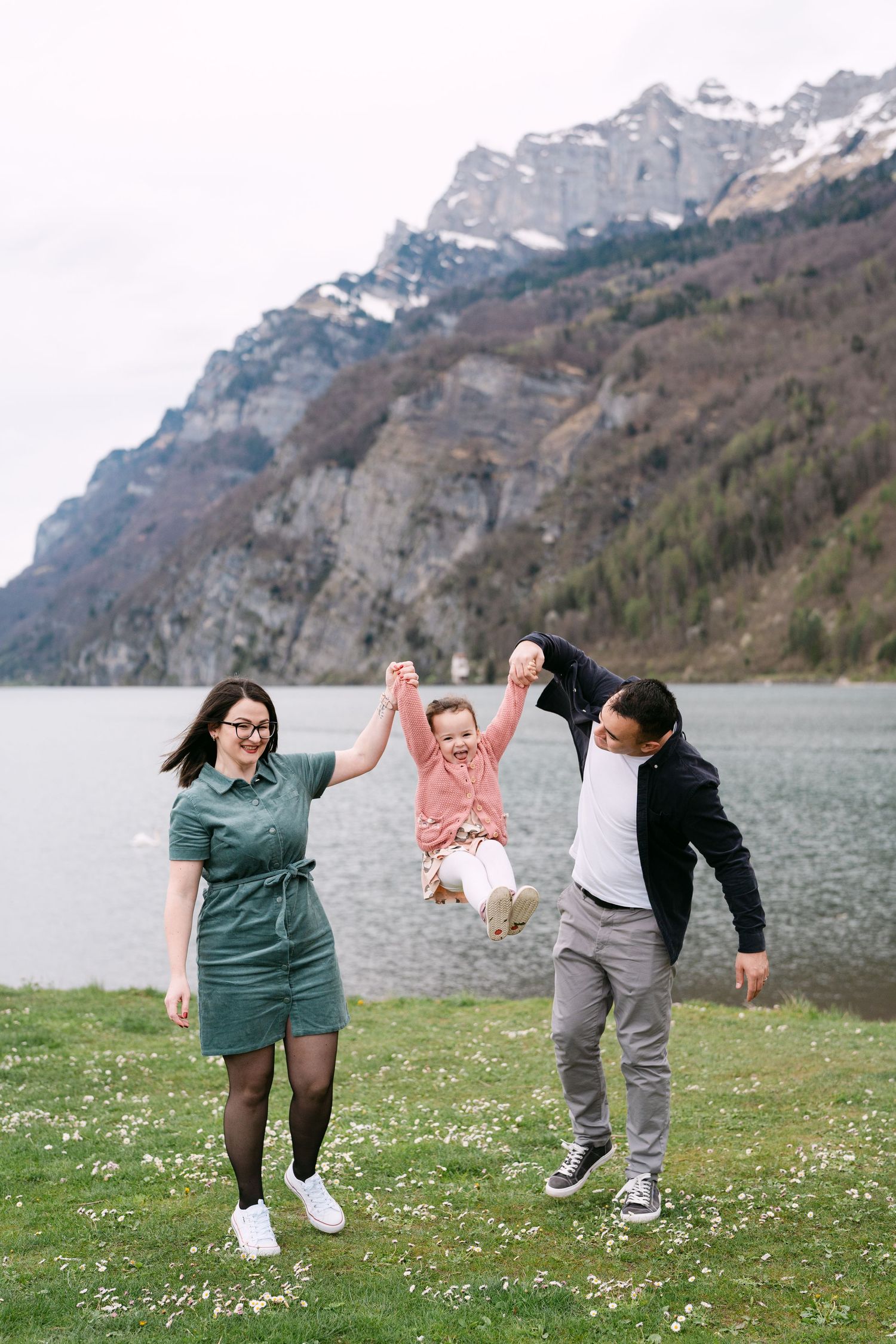 Family playing together in a grassy field with mountains and a lake in the scenic backdrop.