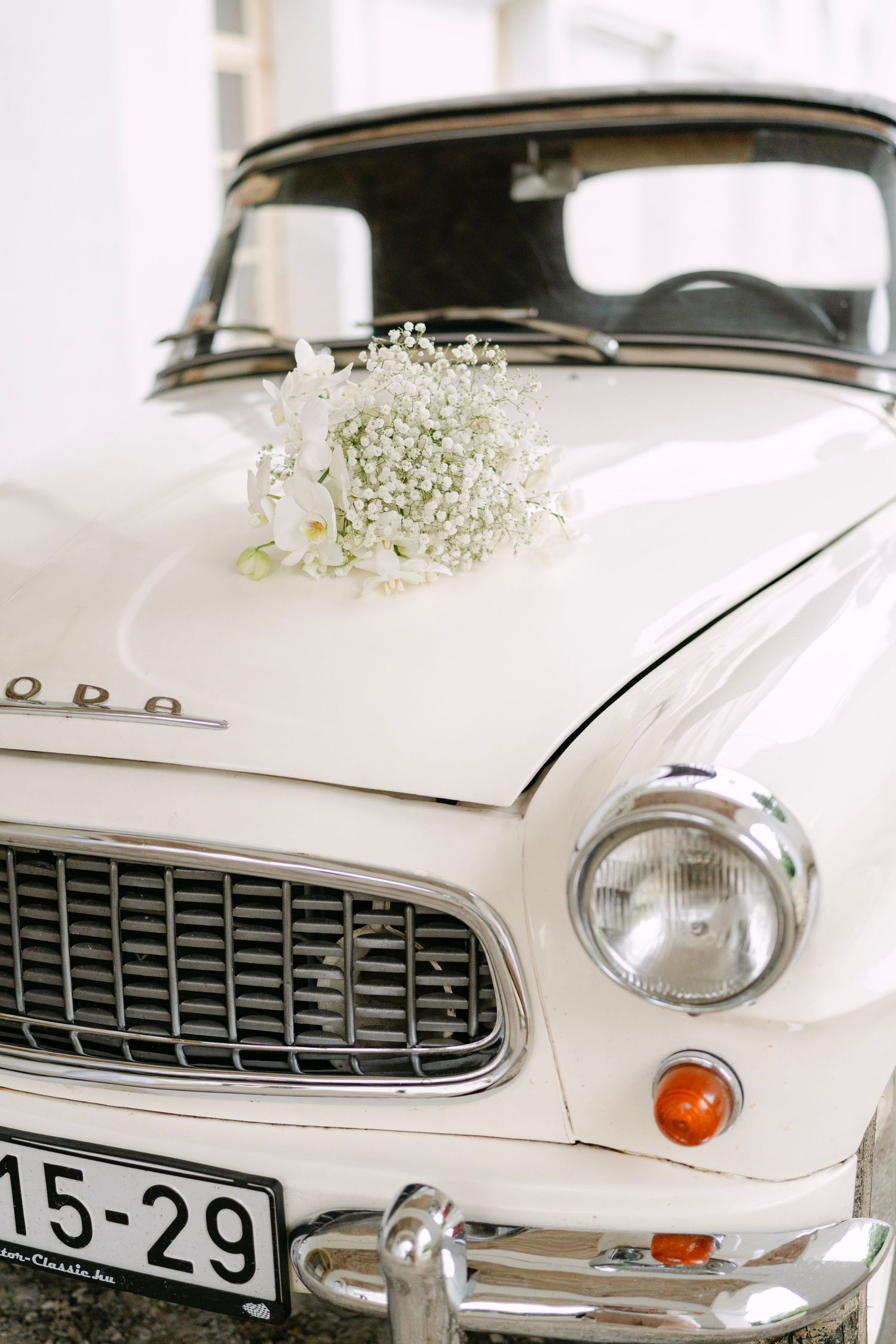 Front view of a classic white vintage car decorated with baby's breath flowers.