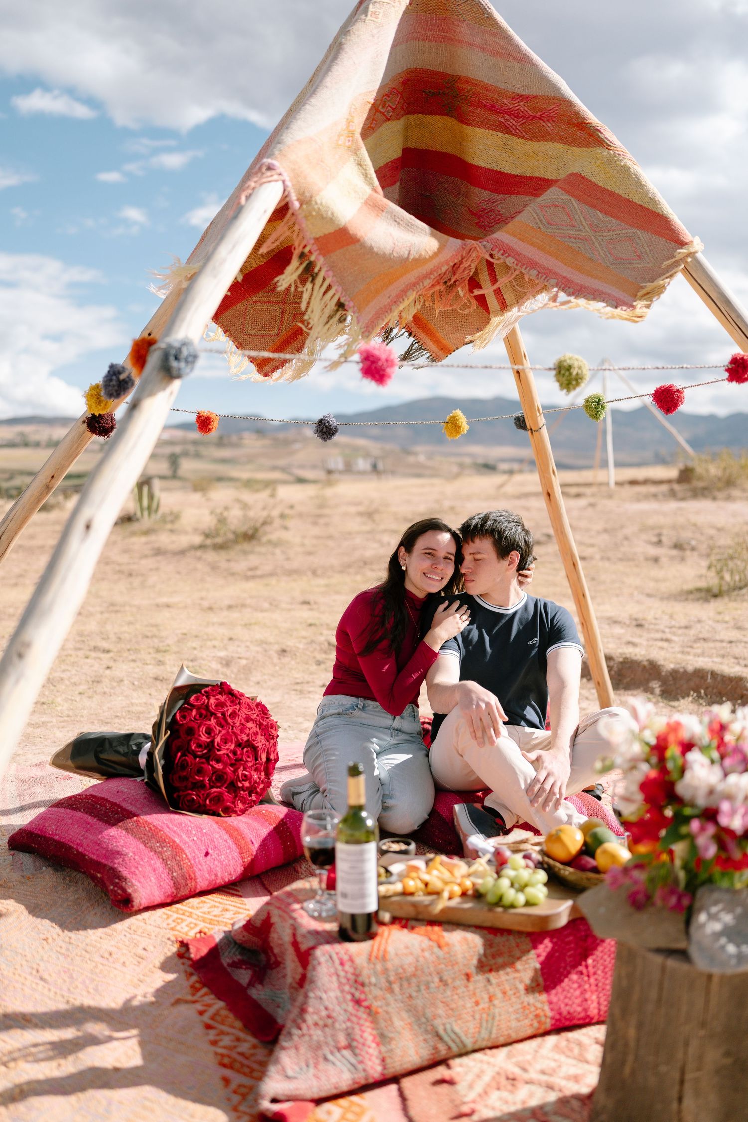 Romantic desert picnic setup with floral arrangements and cozy cushions under a canopy.