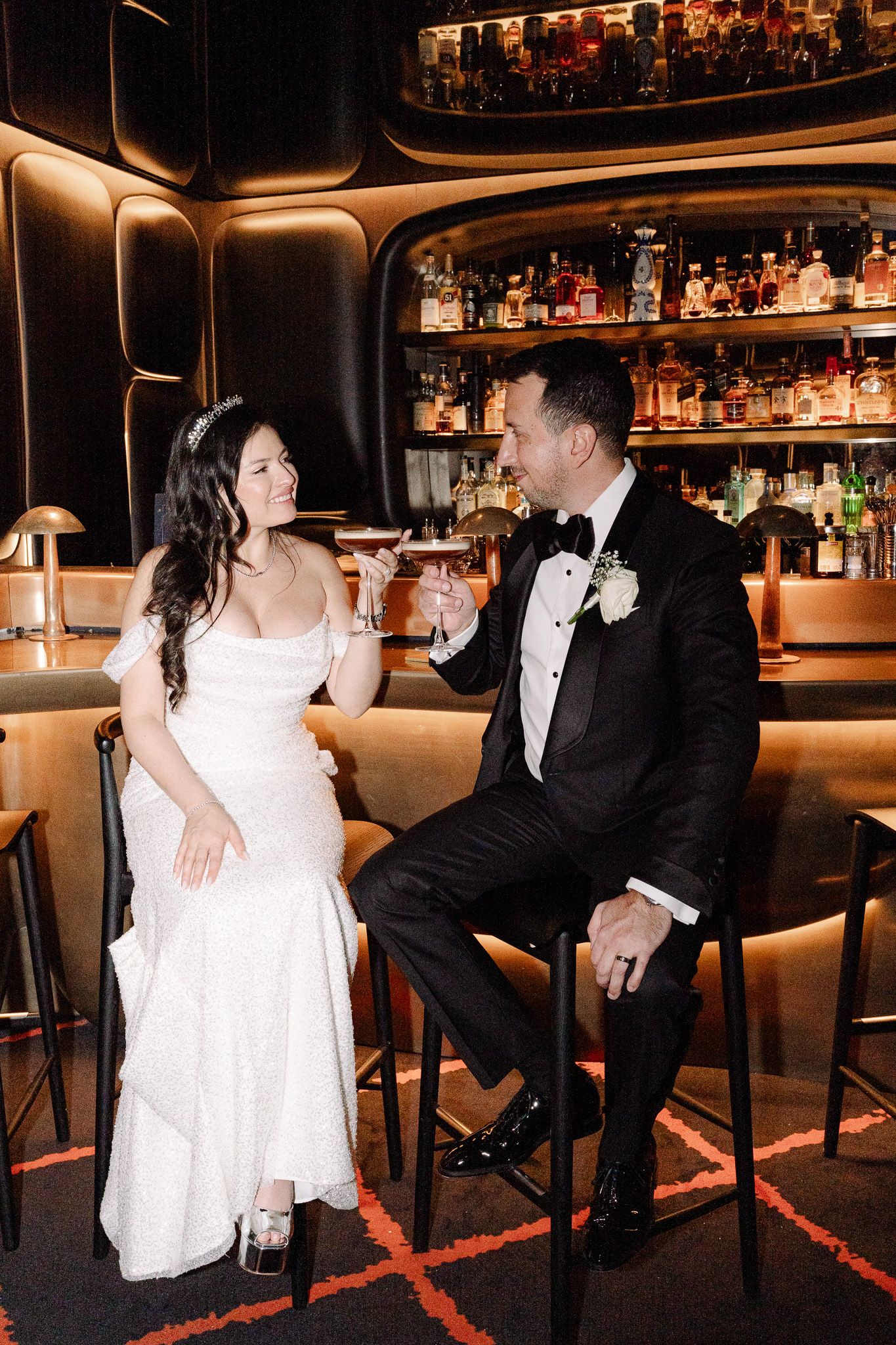 Couple shares drinks at elegant bar in wedding attire.