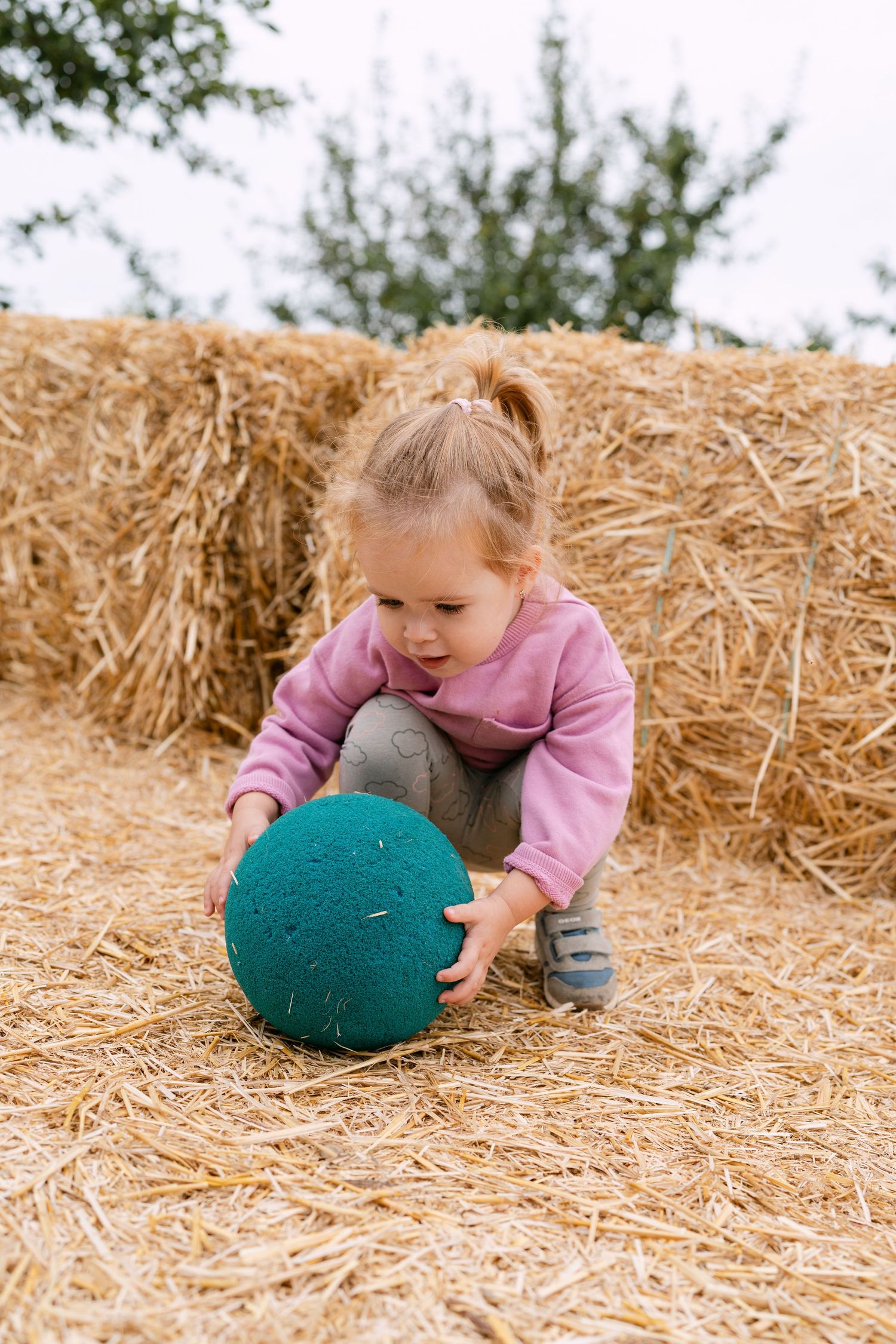 Young child playing with a green cushion on hay bales.