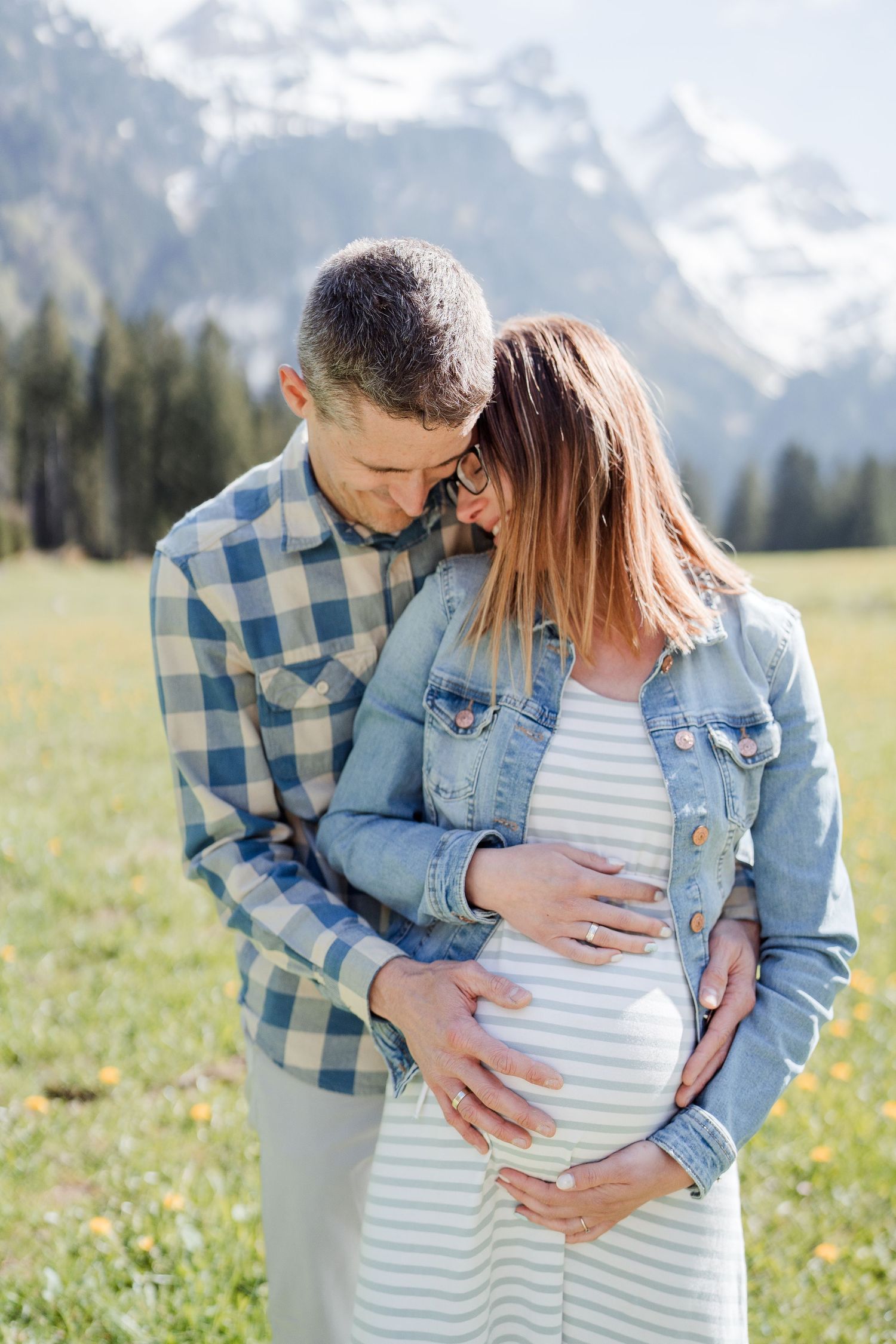 A couple embraces in a meadow with dramatic mountain peaks in the background.