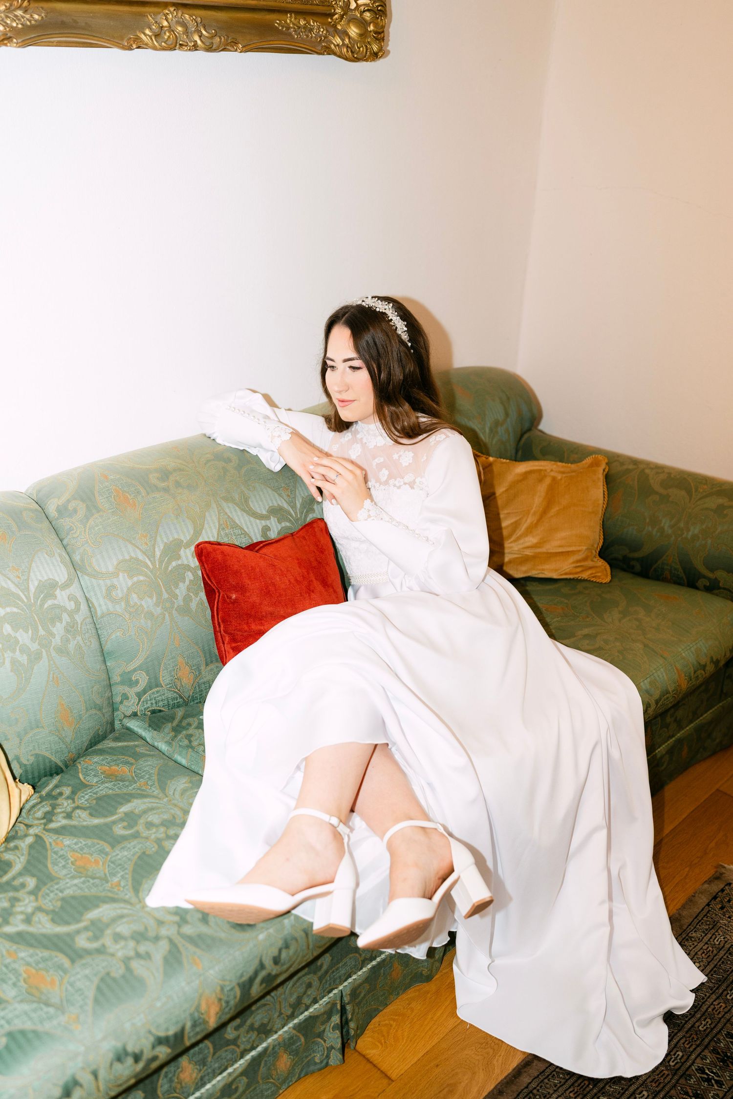 Person in white dress poses dramatically on vintage teal sofa.