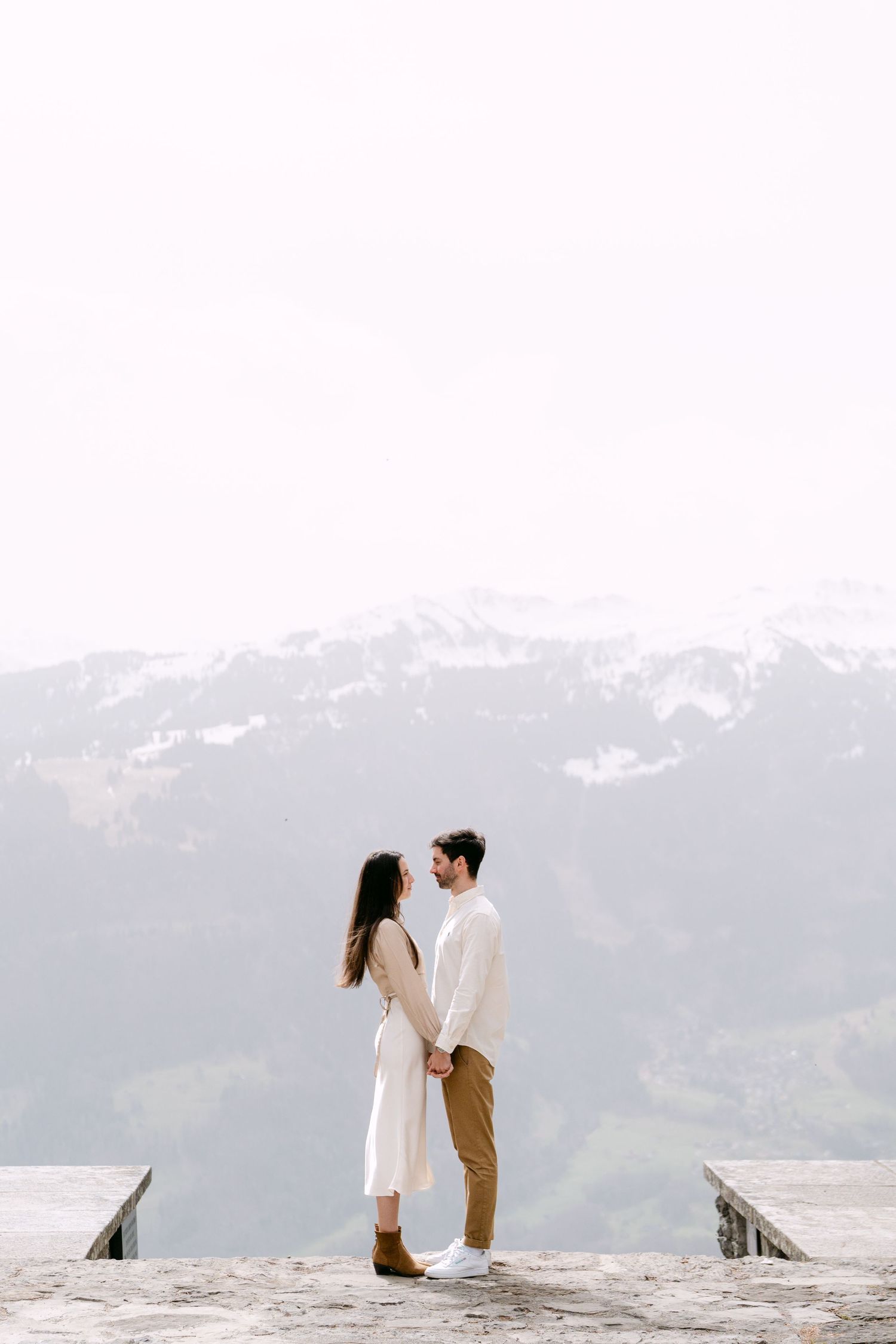 Two people share intimate moments while sitting on a rocky overlook with mountain views.