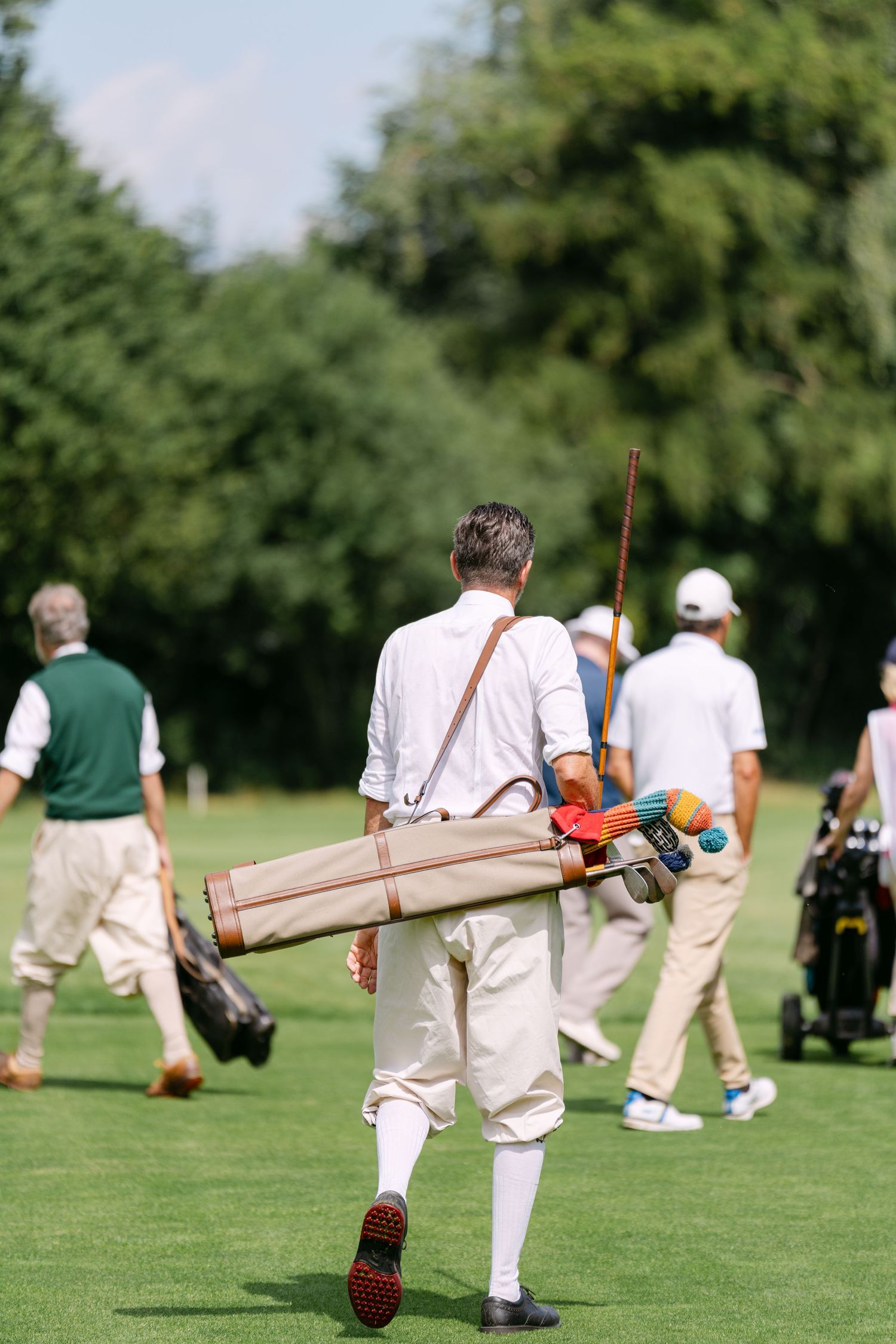 Group of players walking across a croquet lawn carrying mallets and equipment.