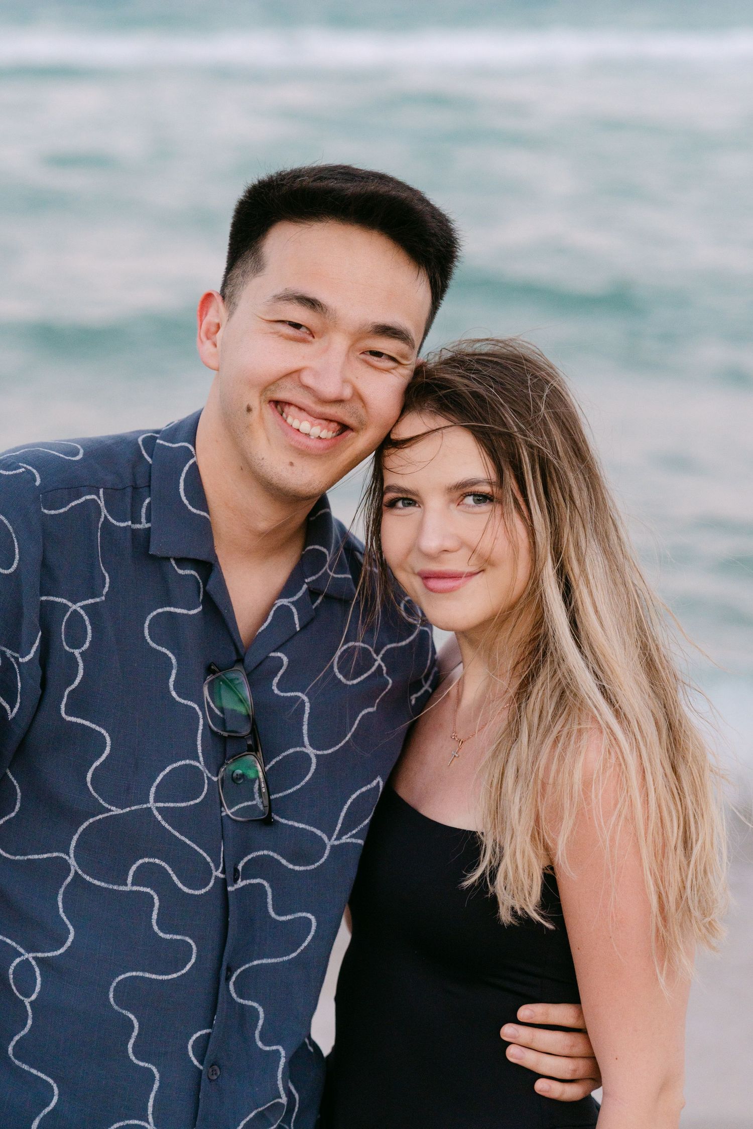 A happy couple embraces on the beach with the ocean waves creating a romantic backdrop.