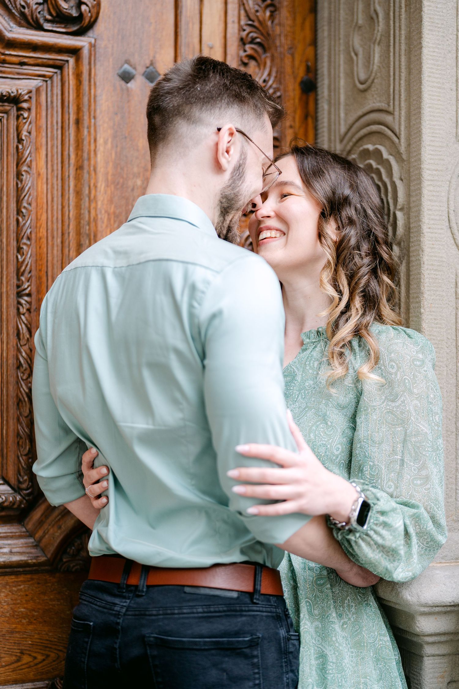 A couple in vintage-inspired outfits shares a romantic moment against an ornate wooden door background.