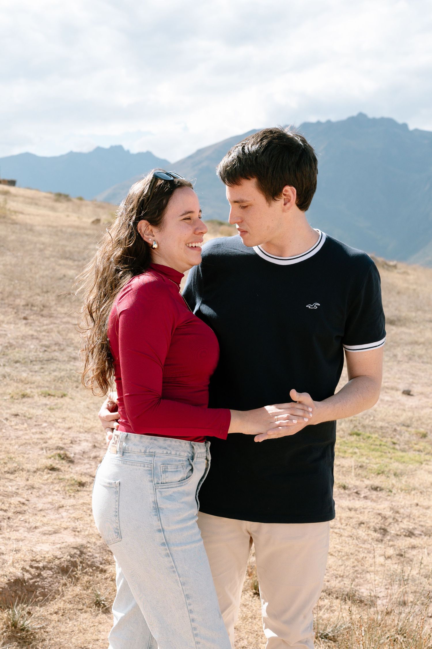 A romantic couple shares intimate moments against a mountainous backdrop wearing red and black outfits.