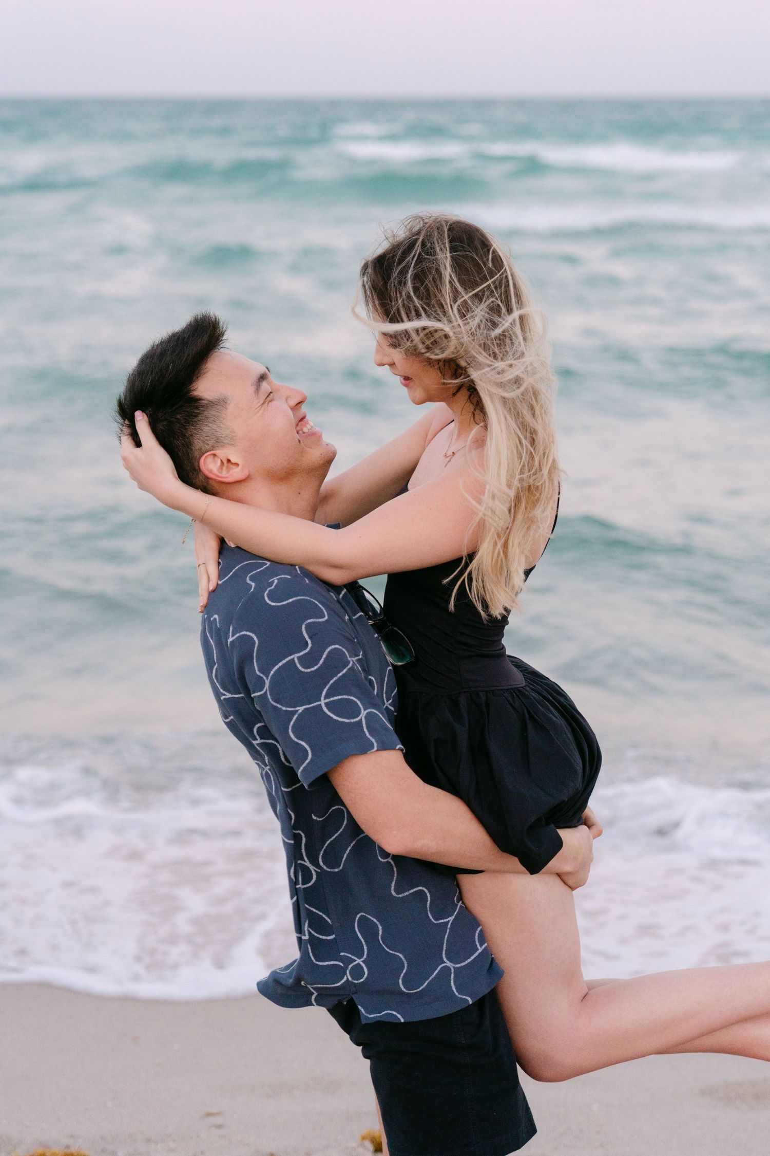 A couple shares playful moments on the beach as one lifts the other in a joyful embrace.